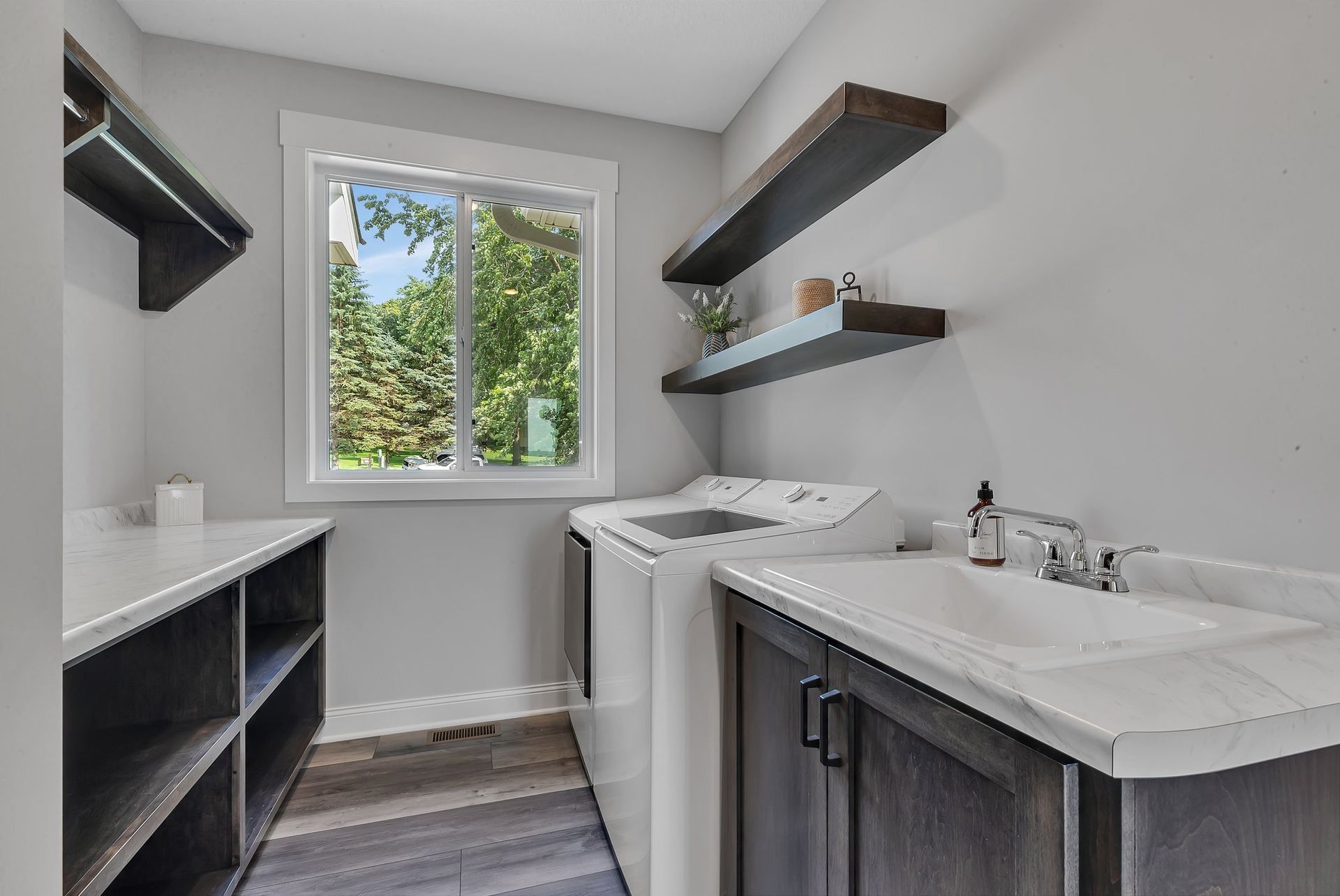 A laundry room with a washer and dryer , sink , shelves and a window.
