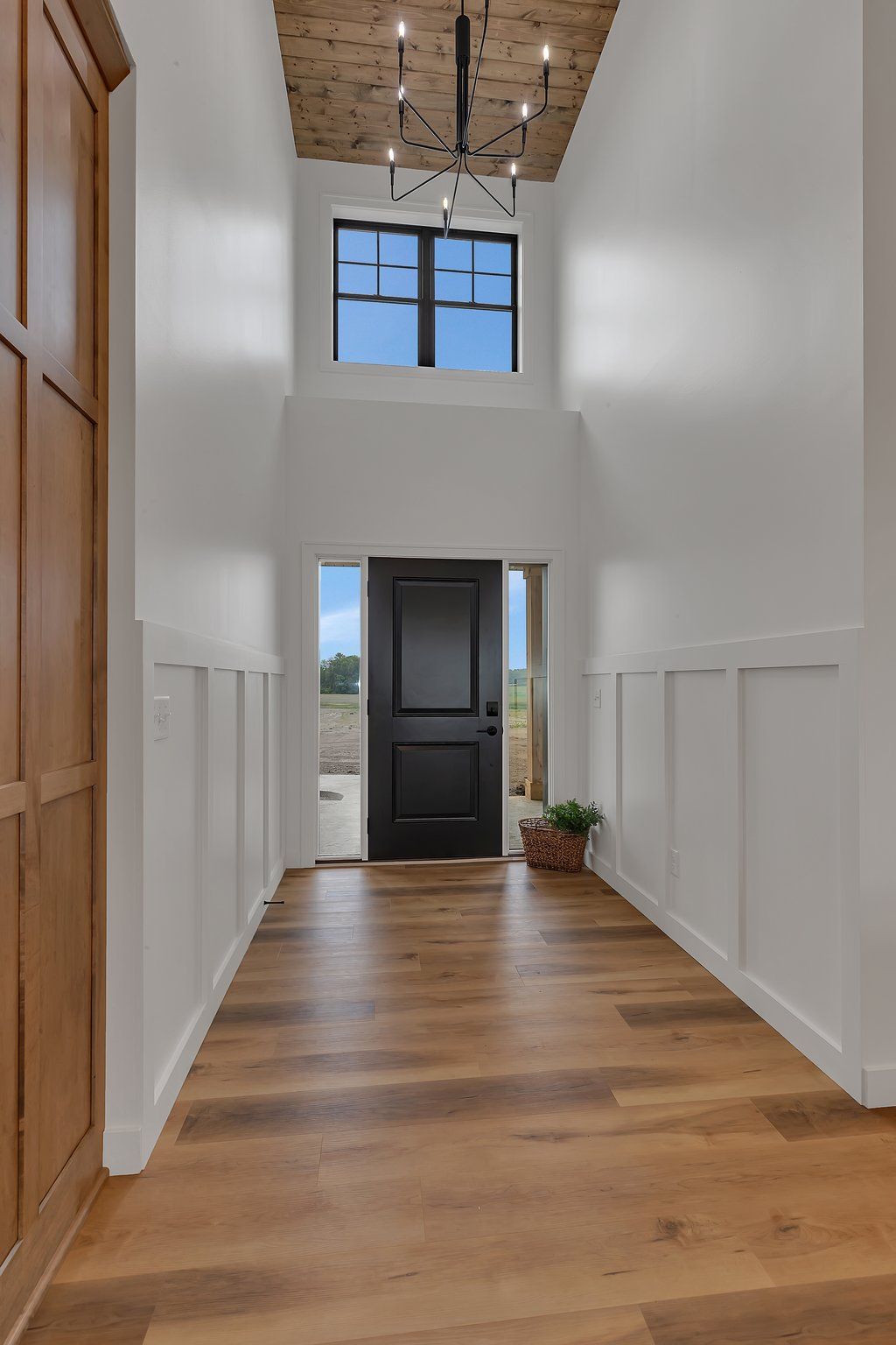 A hallway in a house with a black door and a chandelier.