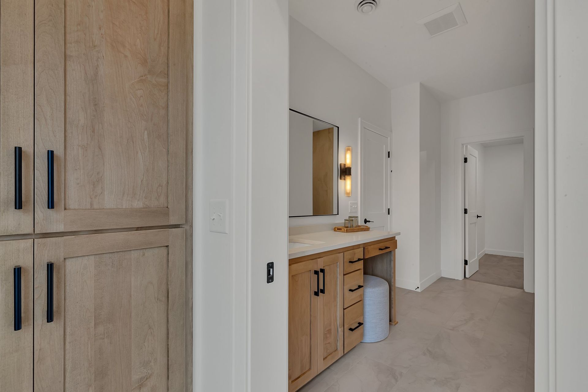 A bathroom with wooden cabinets , a vanity , a mirror and a stool.