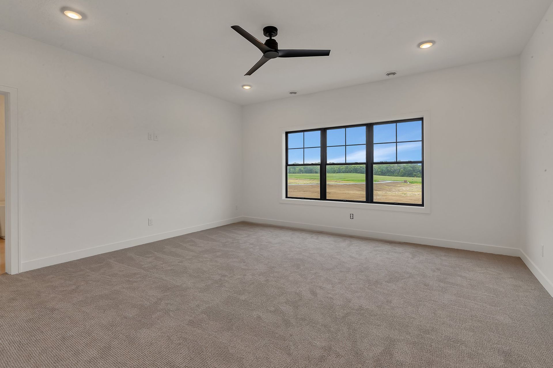 A large empty room with a ceiling fan and two windows.