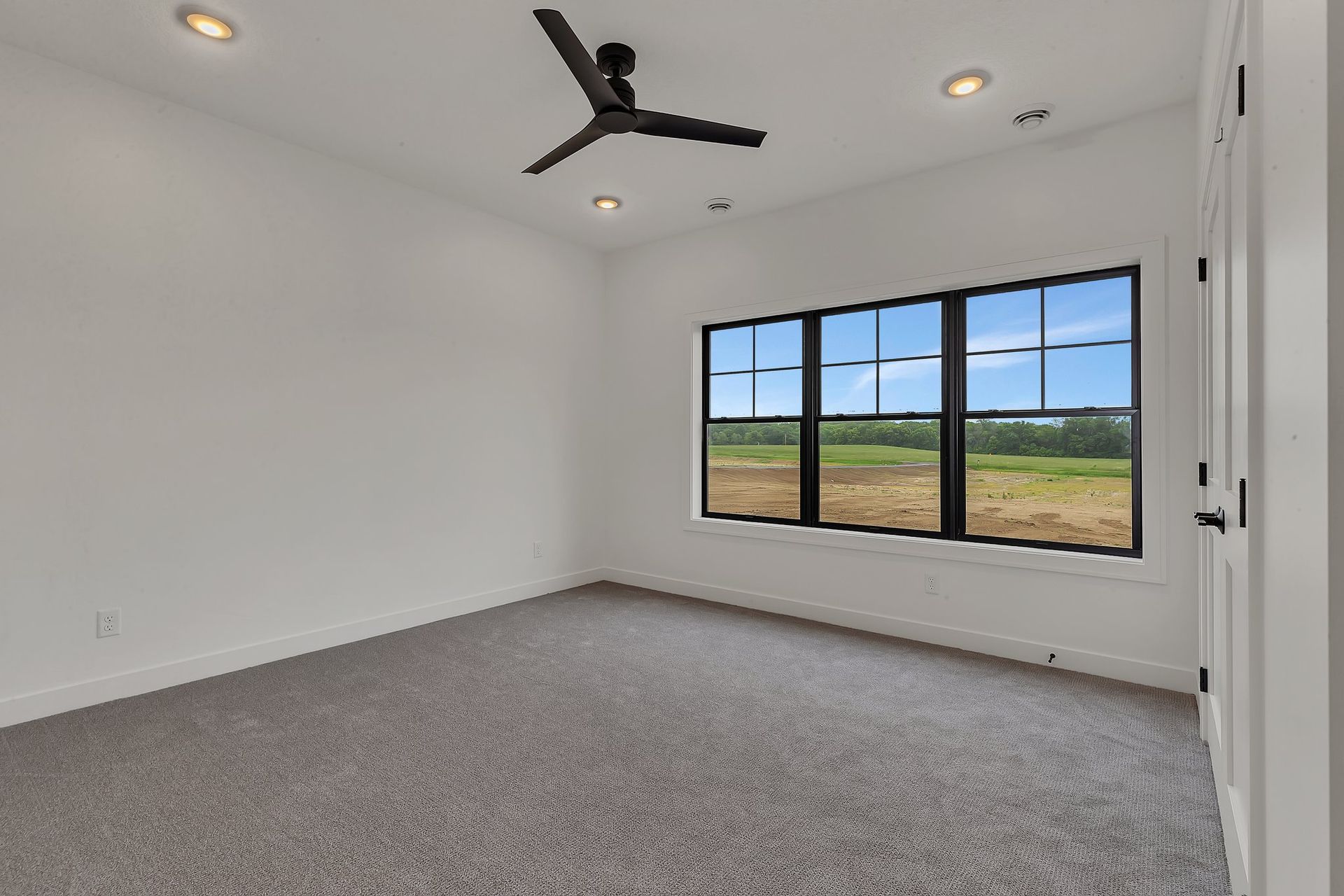 An empty bedroom with a ceiling fan and three windows.