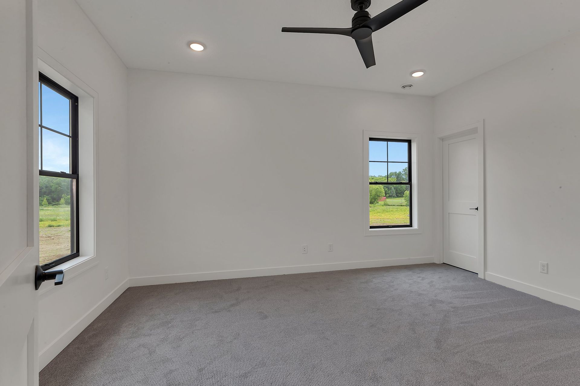 An empty bedroom with a ceiling fan and two windows.