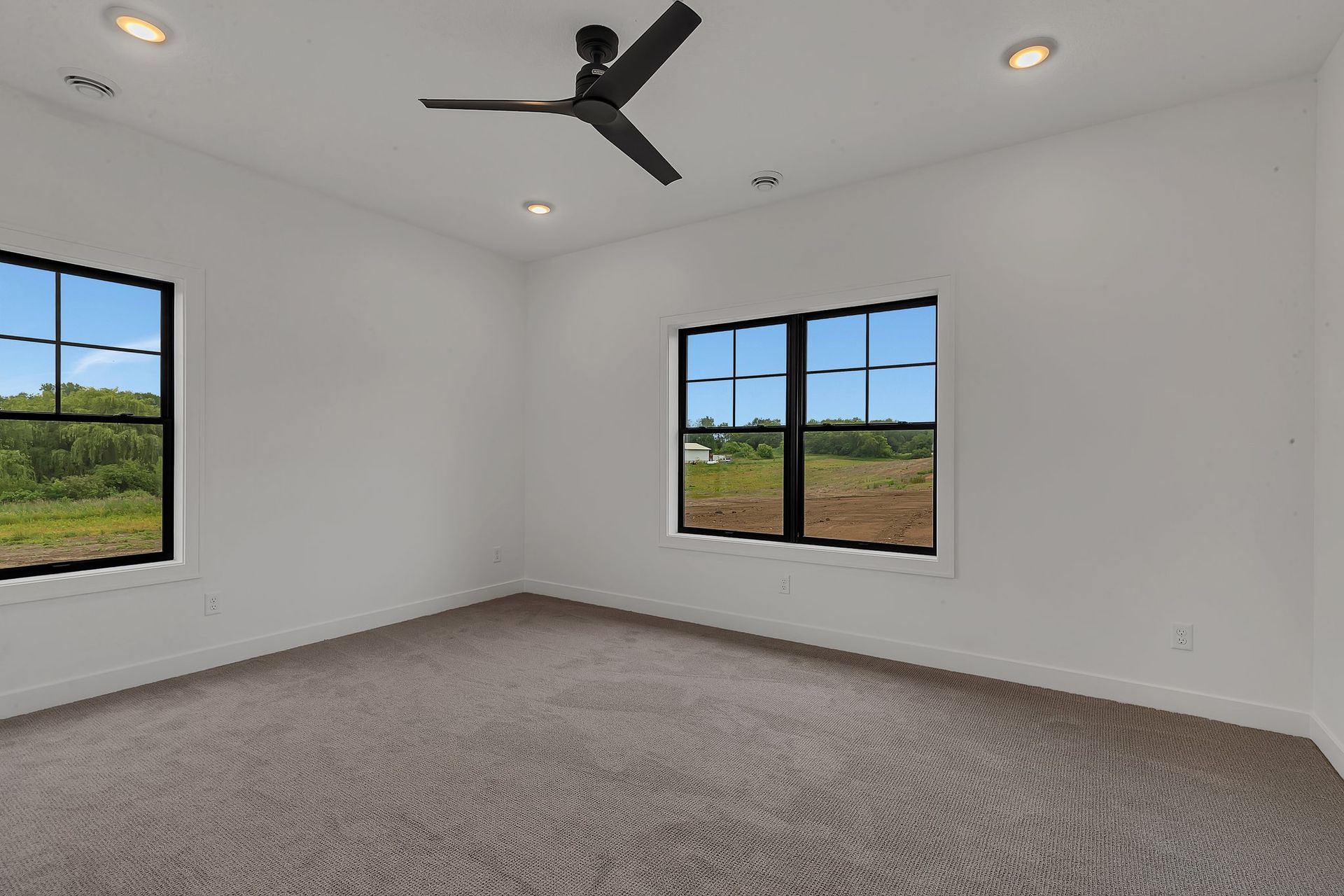 An empty bedroom with a ceiling fan and two windows.