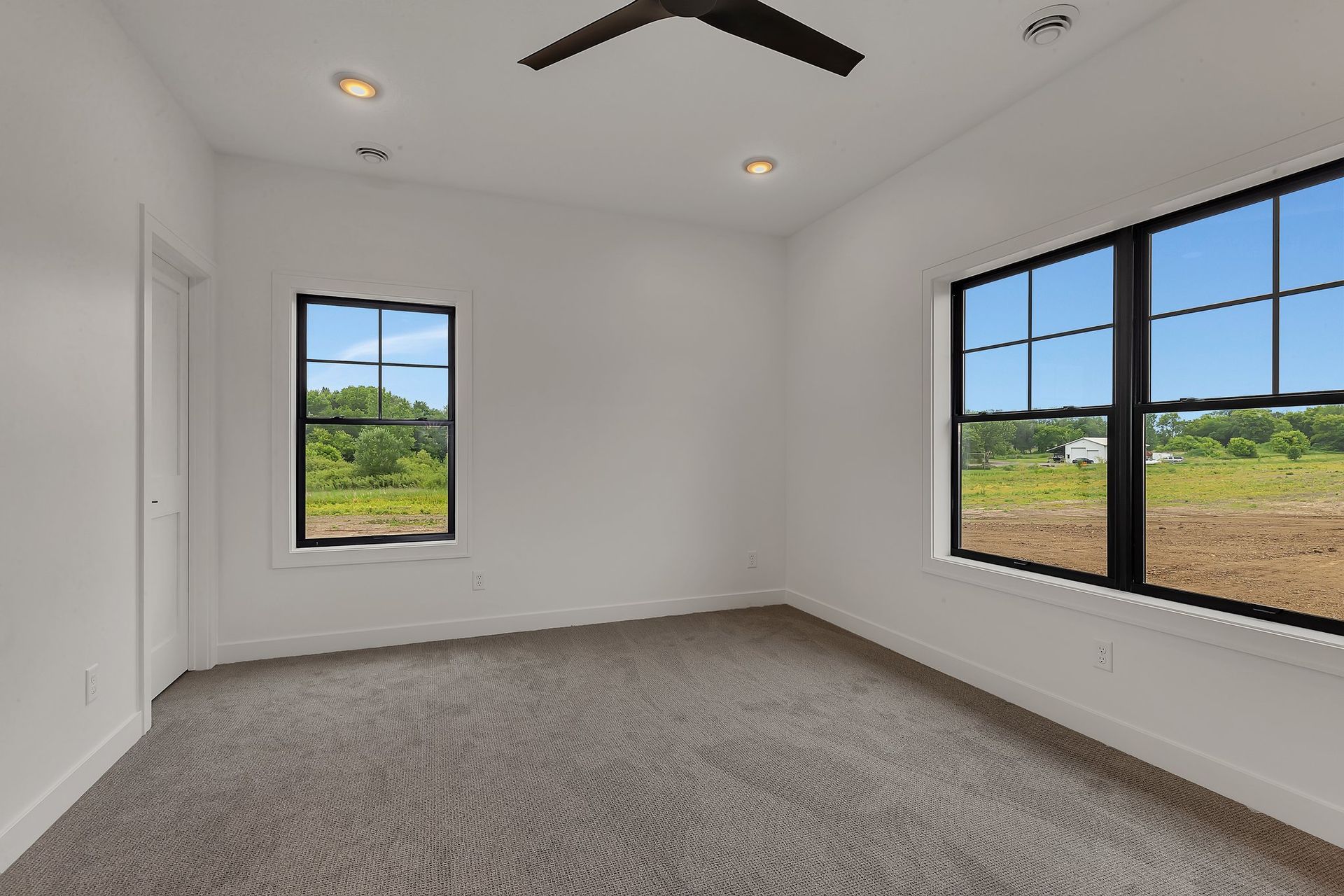 An empty bedroom with two windows and a ceiling fan.