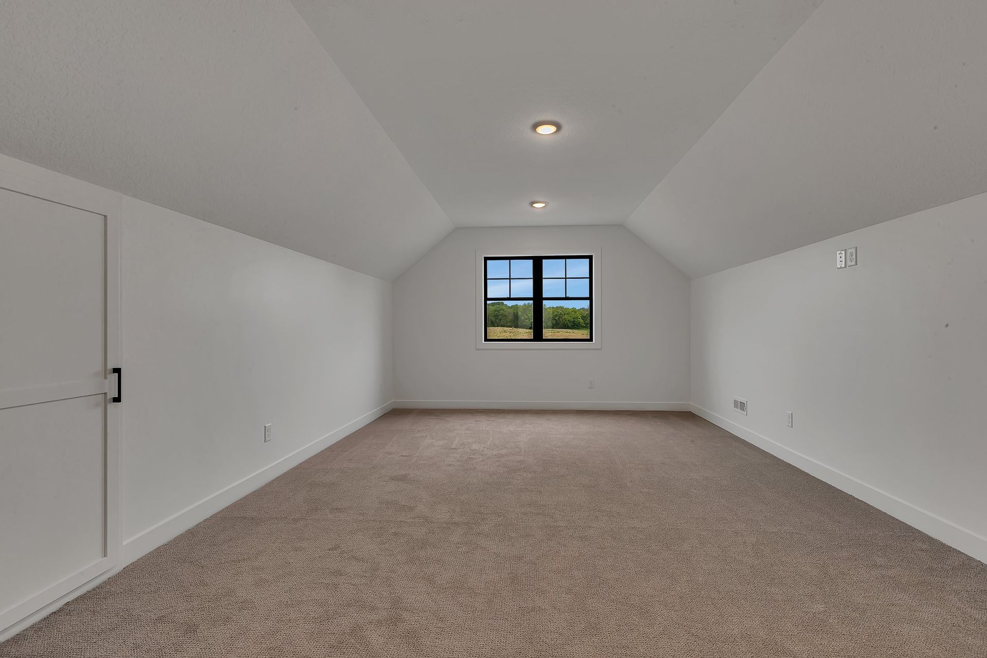 An empty attic with a window and carpet.