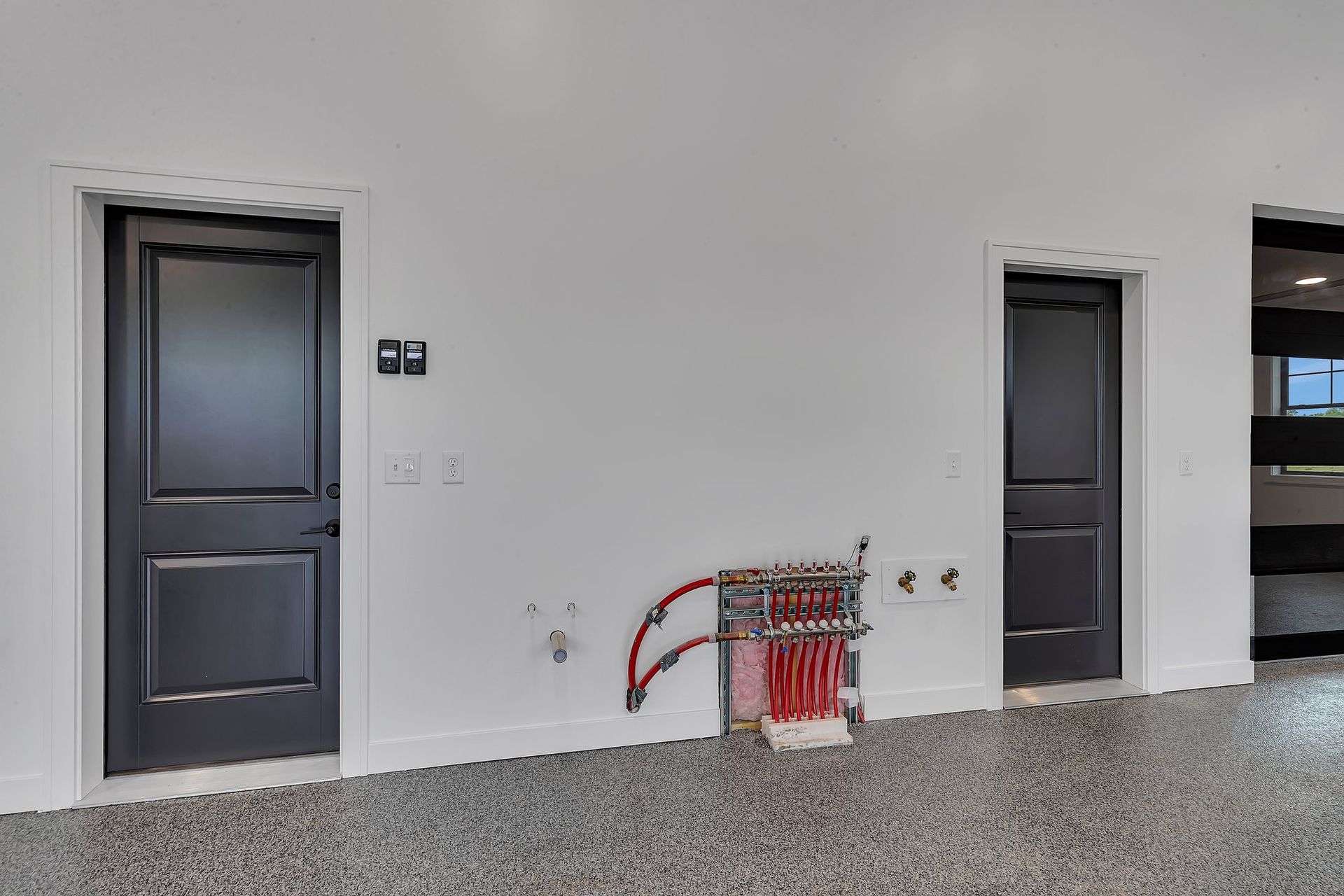 A room with two black doors and a red pipe on the floor.