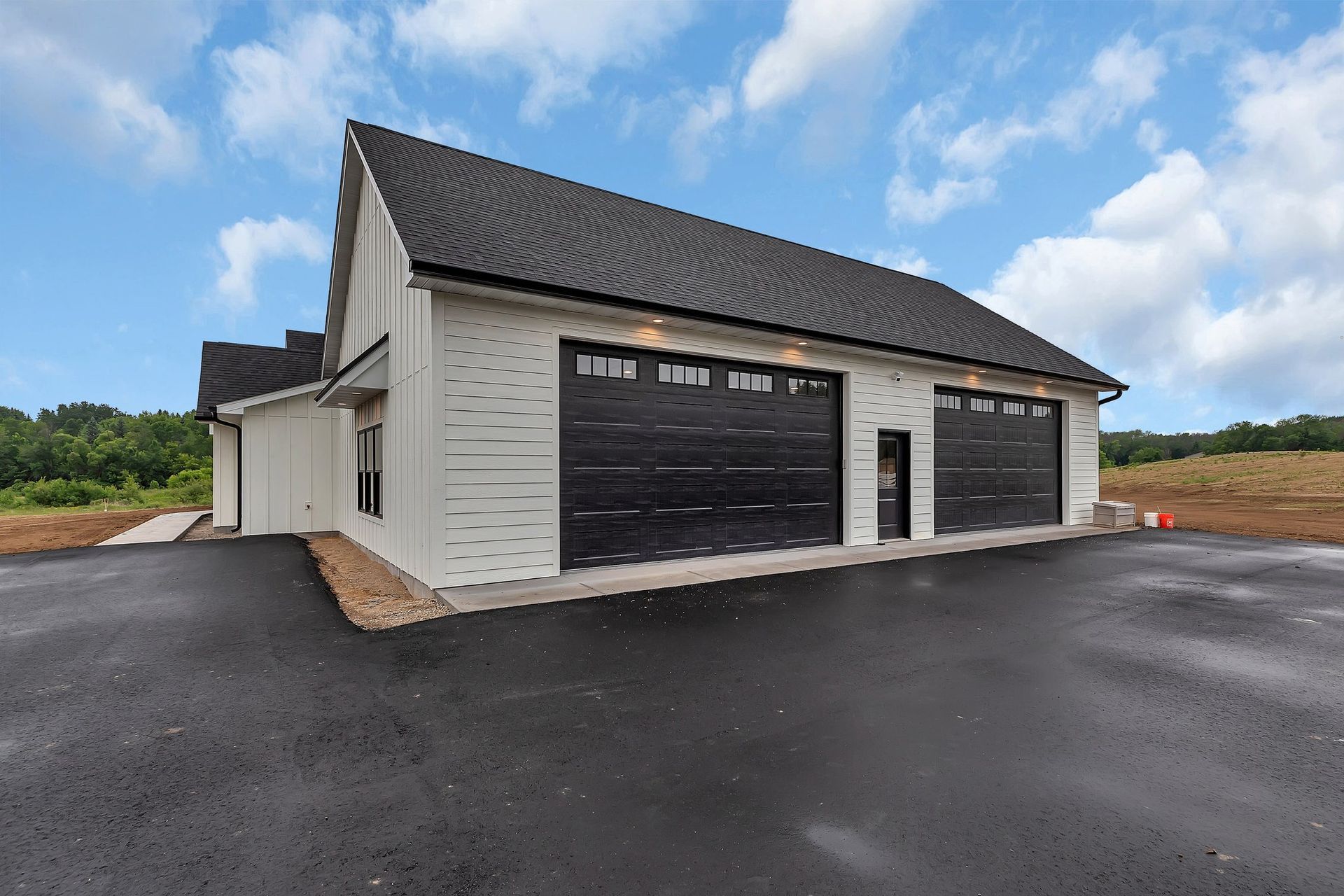 A large white house with black garage doors and a black driveway.