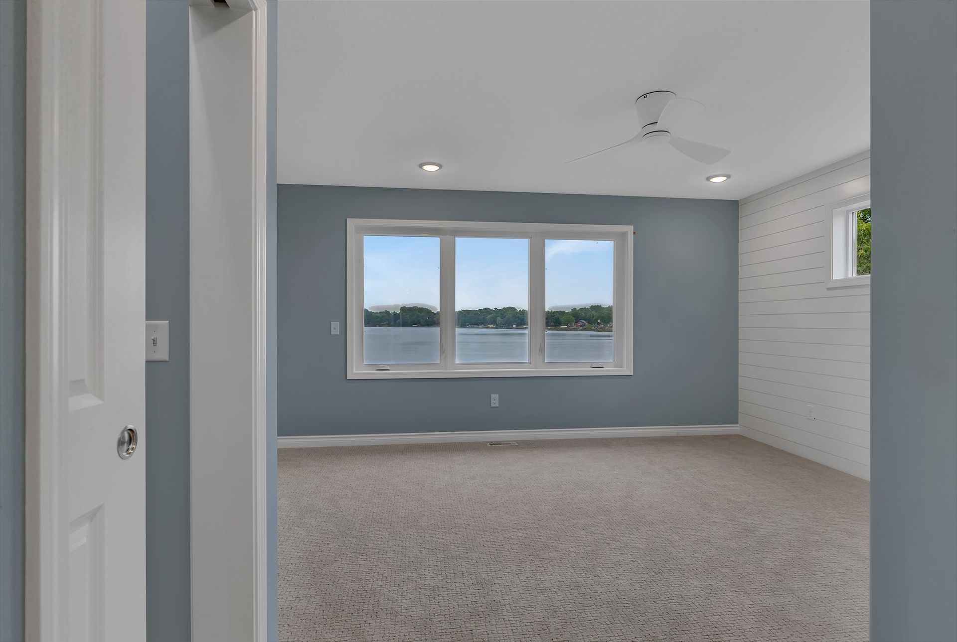 An empty bedroom with a view of a lake and a ceiling fan.