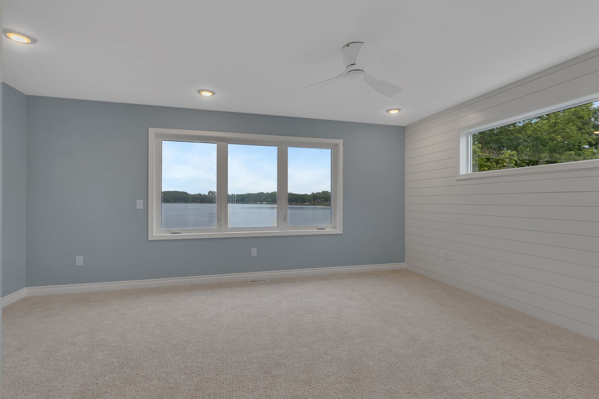 An empty room with two windows and a ceiling fan.