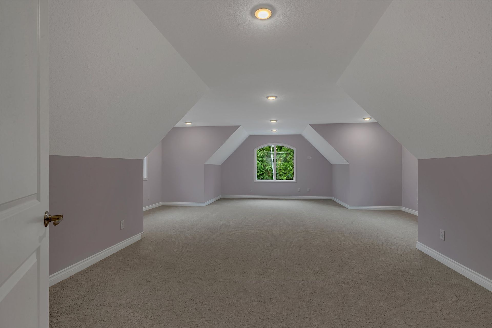 An empty attic with a window and a carpeted floor.