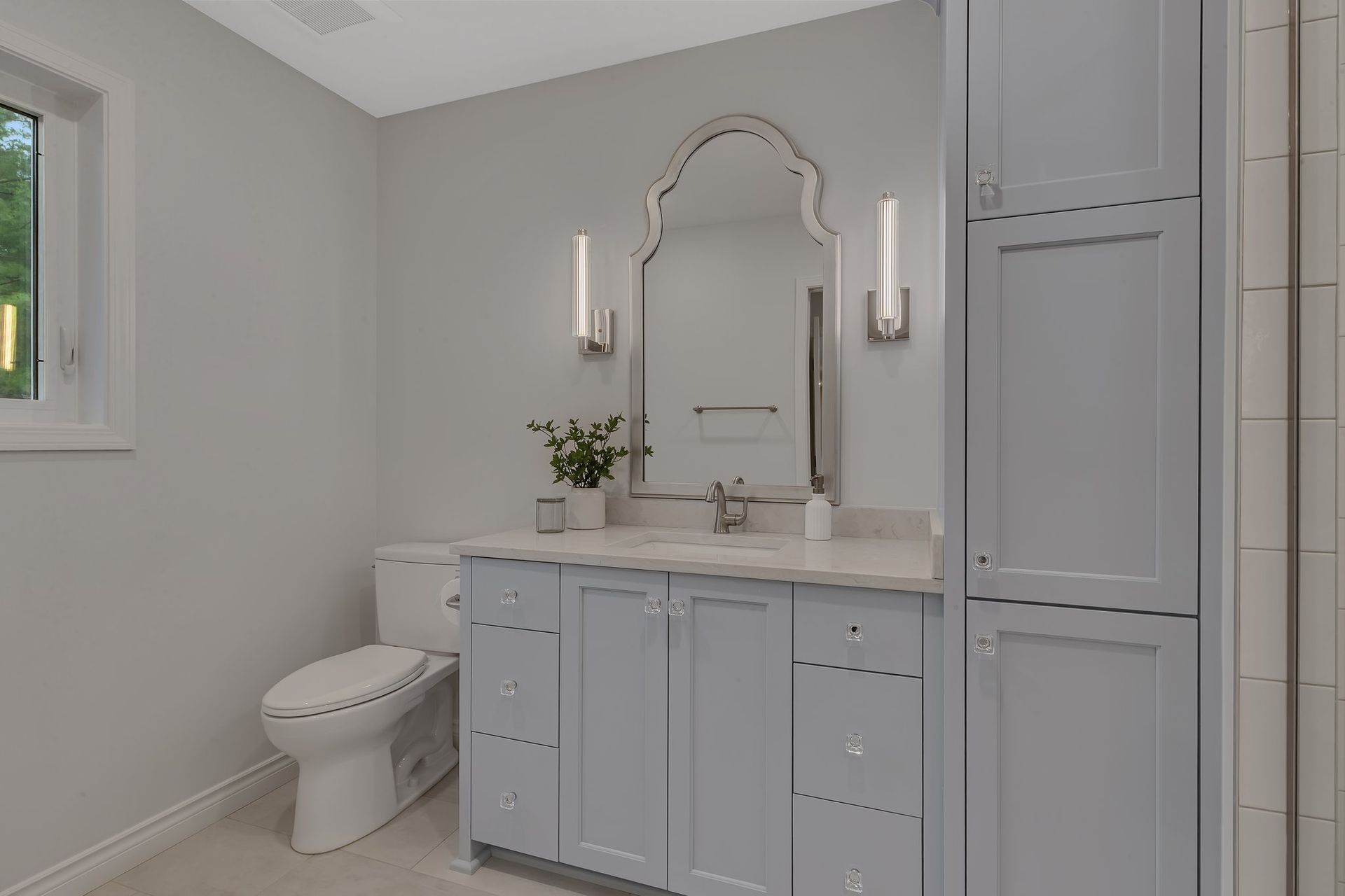 A bathroom with a toilet , sink , mirror and cabinets.