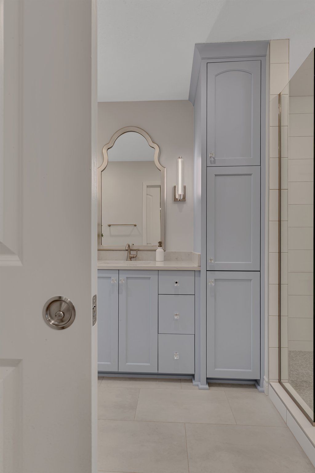 A bathroom with a sink , mirror , cabinets and a walk in shower.