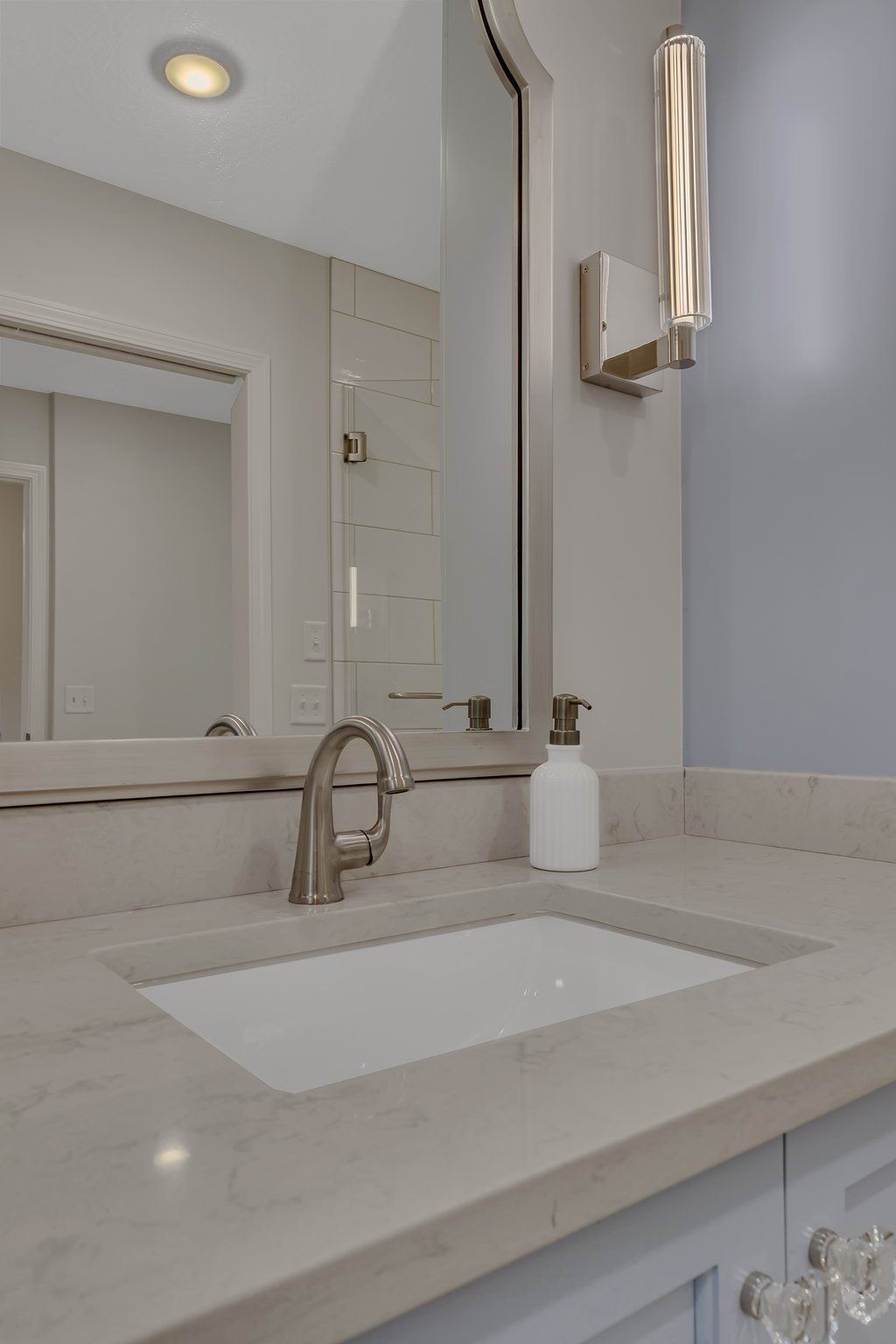 A bathroom with a sink , mirror and soap dispenser.