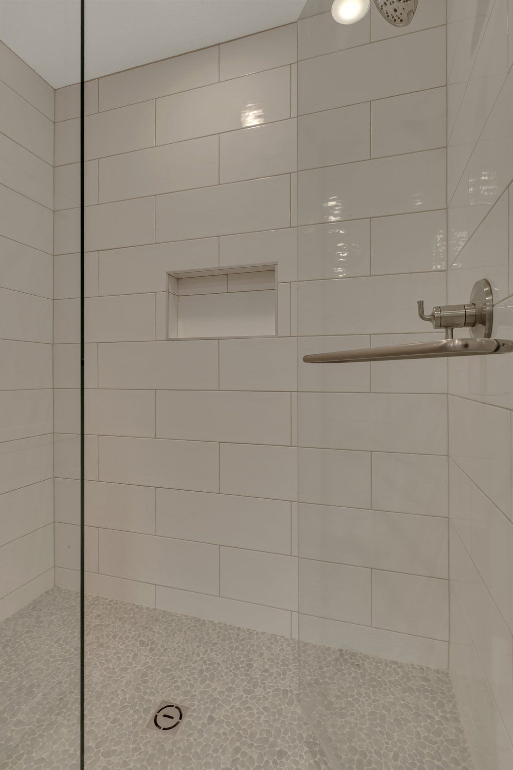 A walk in shower with white tiles and a glass door.