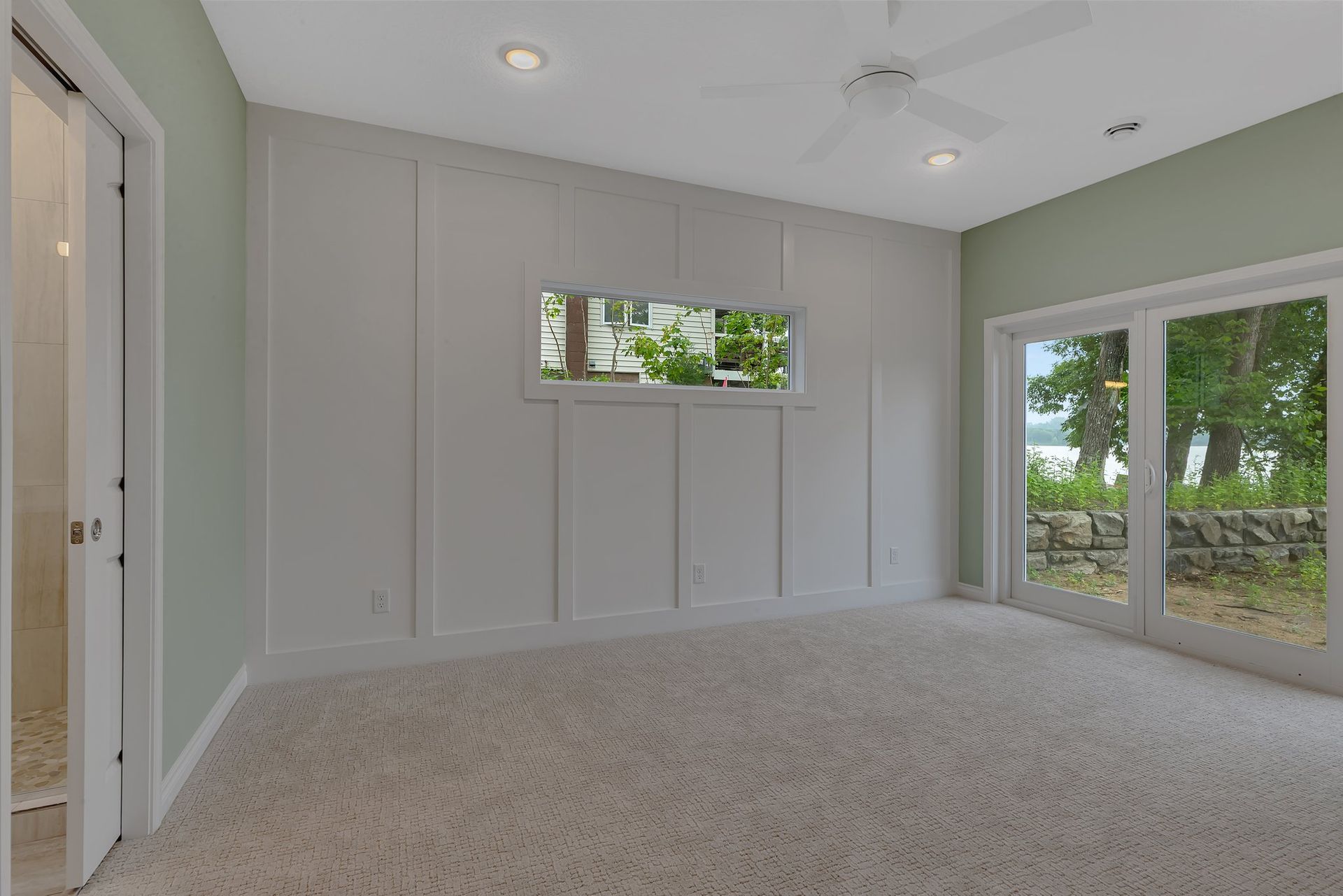 An empty room with a ceiling fan and sliding glass doors.