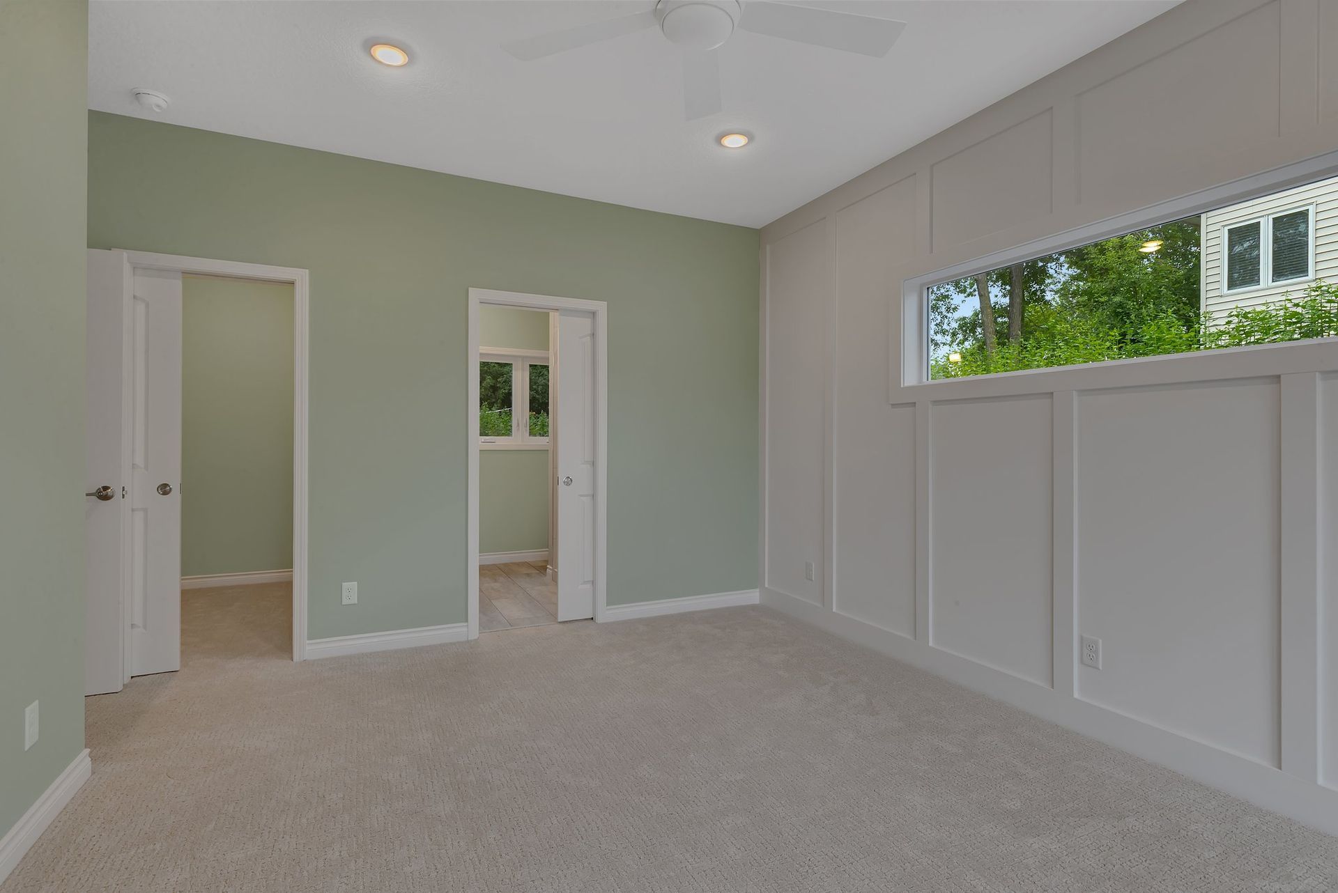 An empty bedroom with a large window and a ceiling fan.