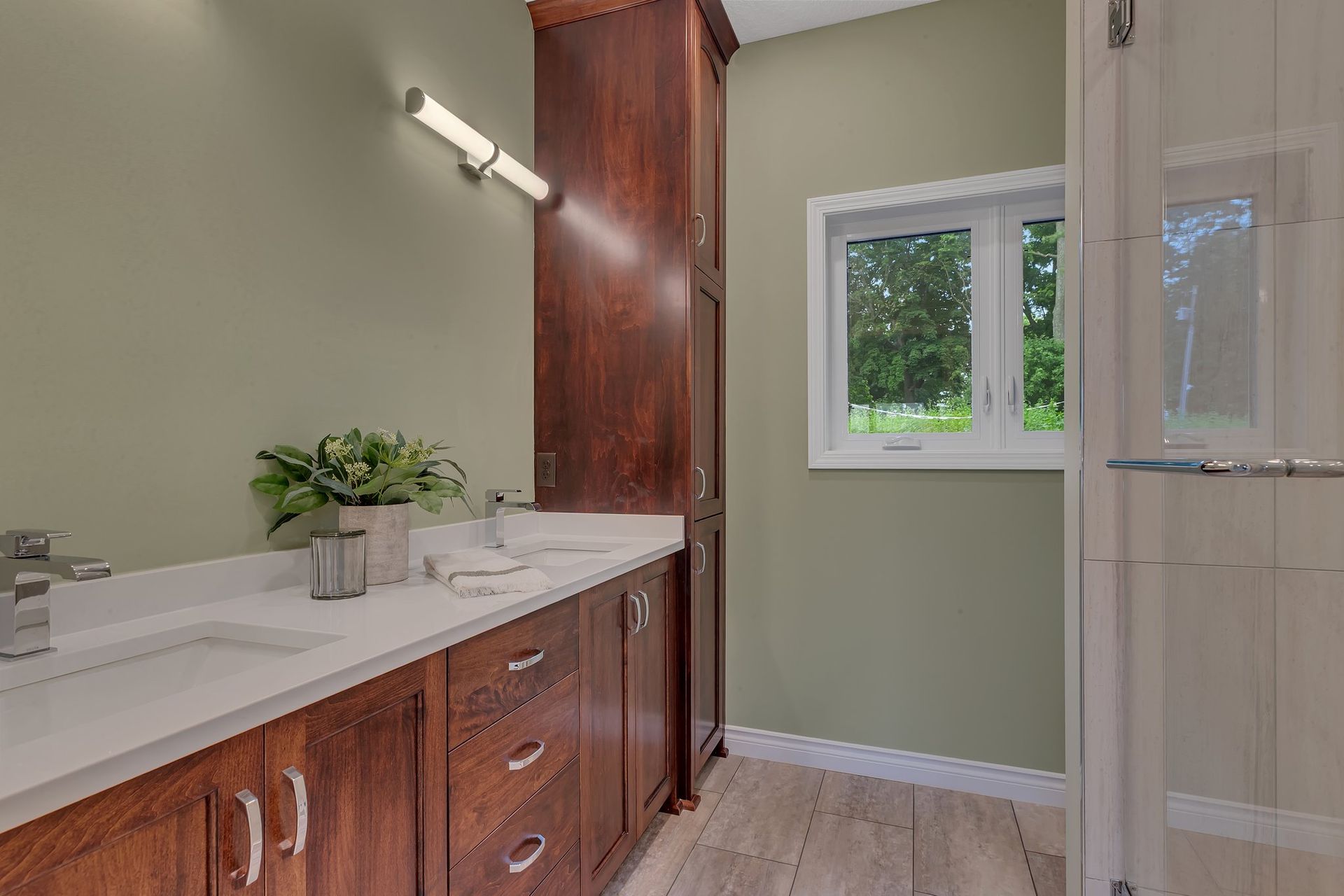 A bathroom with two sinks , a window and a walk in shower.