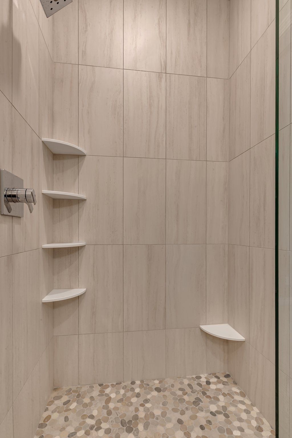 A walk in shower with a tiled floor and shelves.