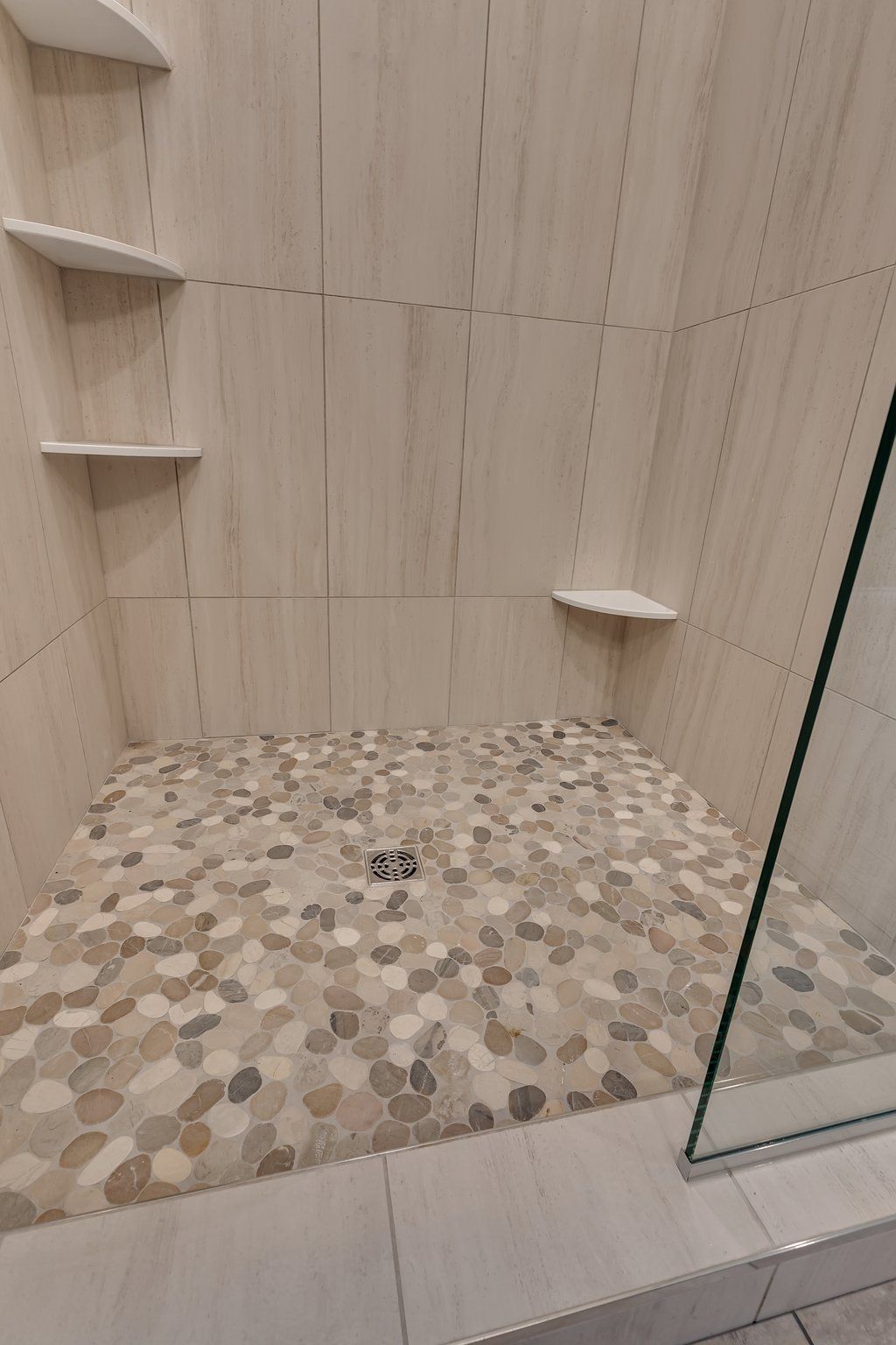 A walk in shower with a tiled floor and shelves.