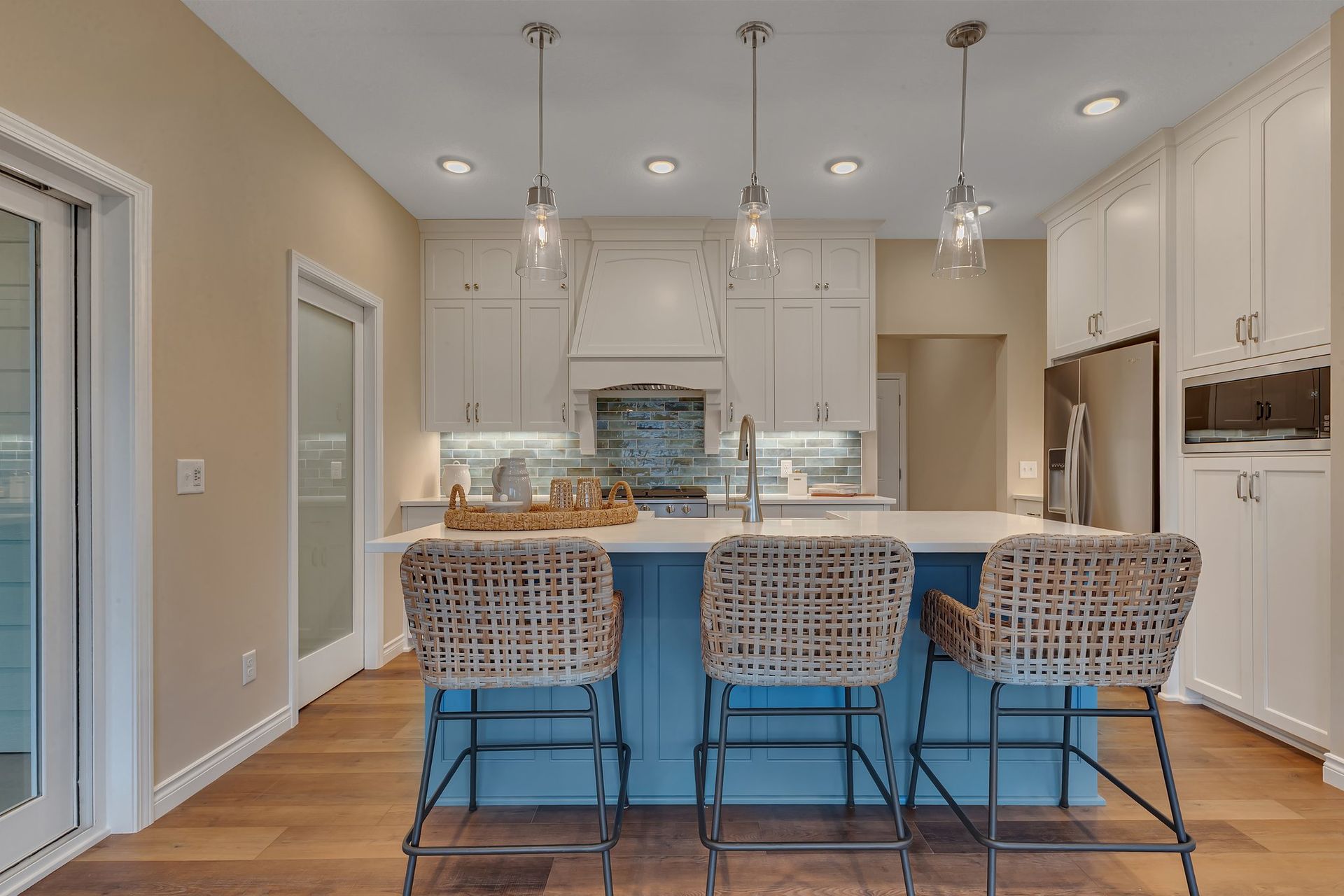 A kitchen with a blue island and wicker chairs.