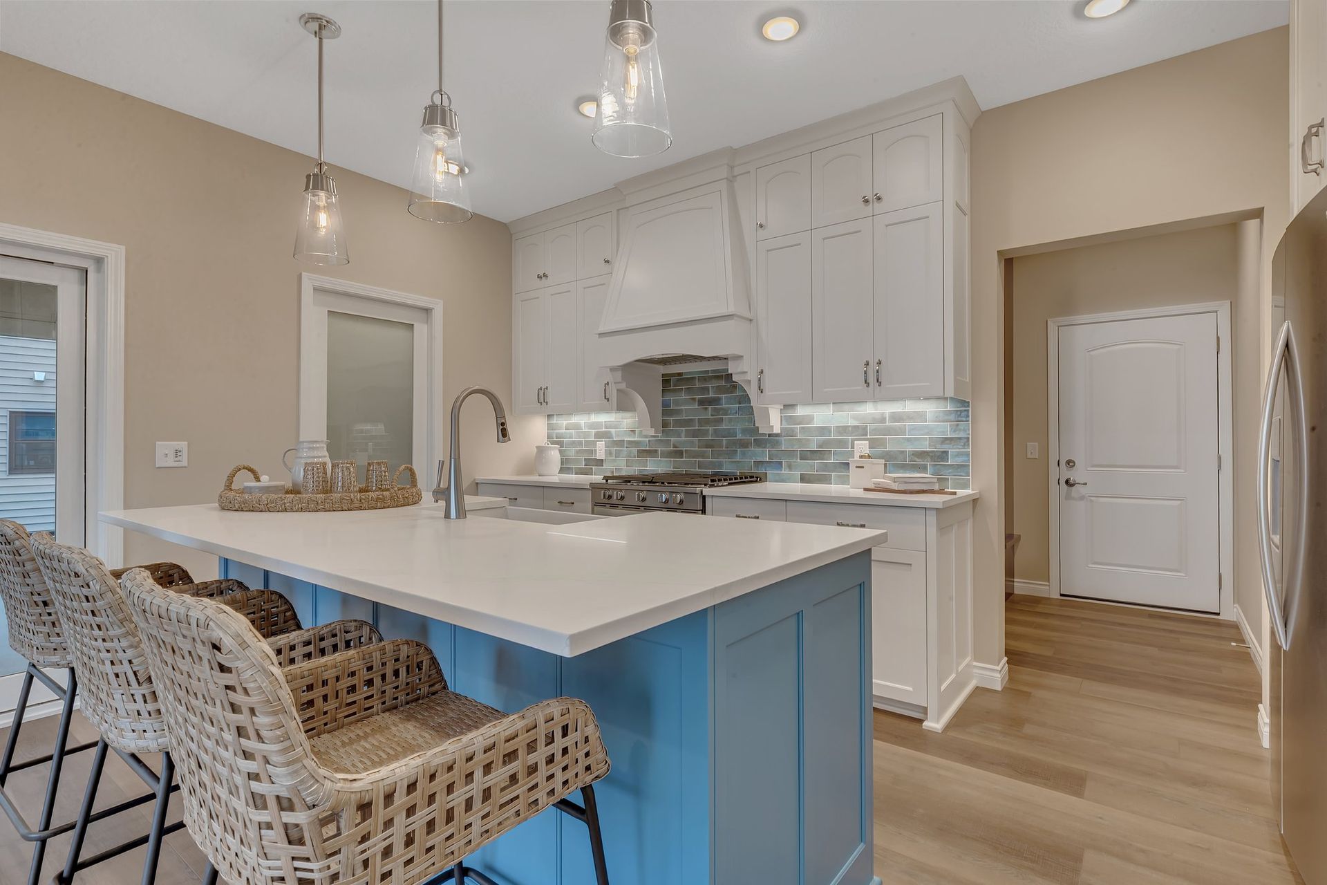 A kitchen with blue cabinets , white counter tops , and wicker chairs.
