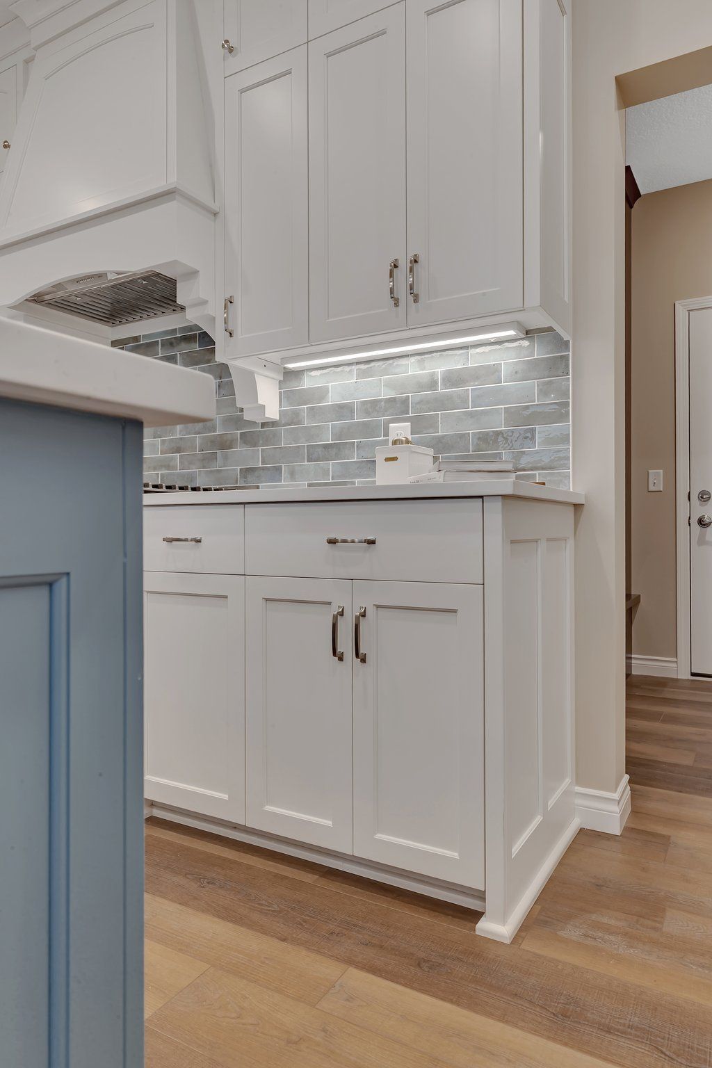 A kitchen with white cabinets and blue cabinets and a wooden floor.