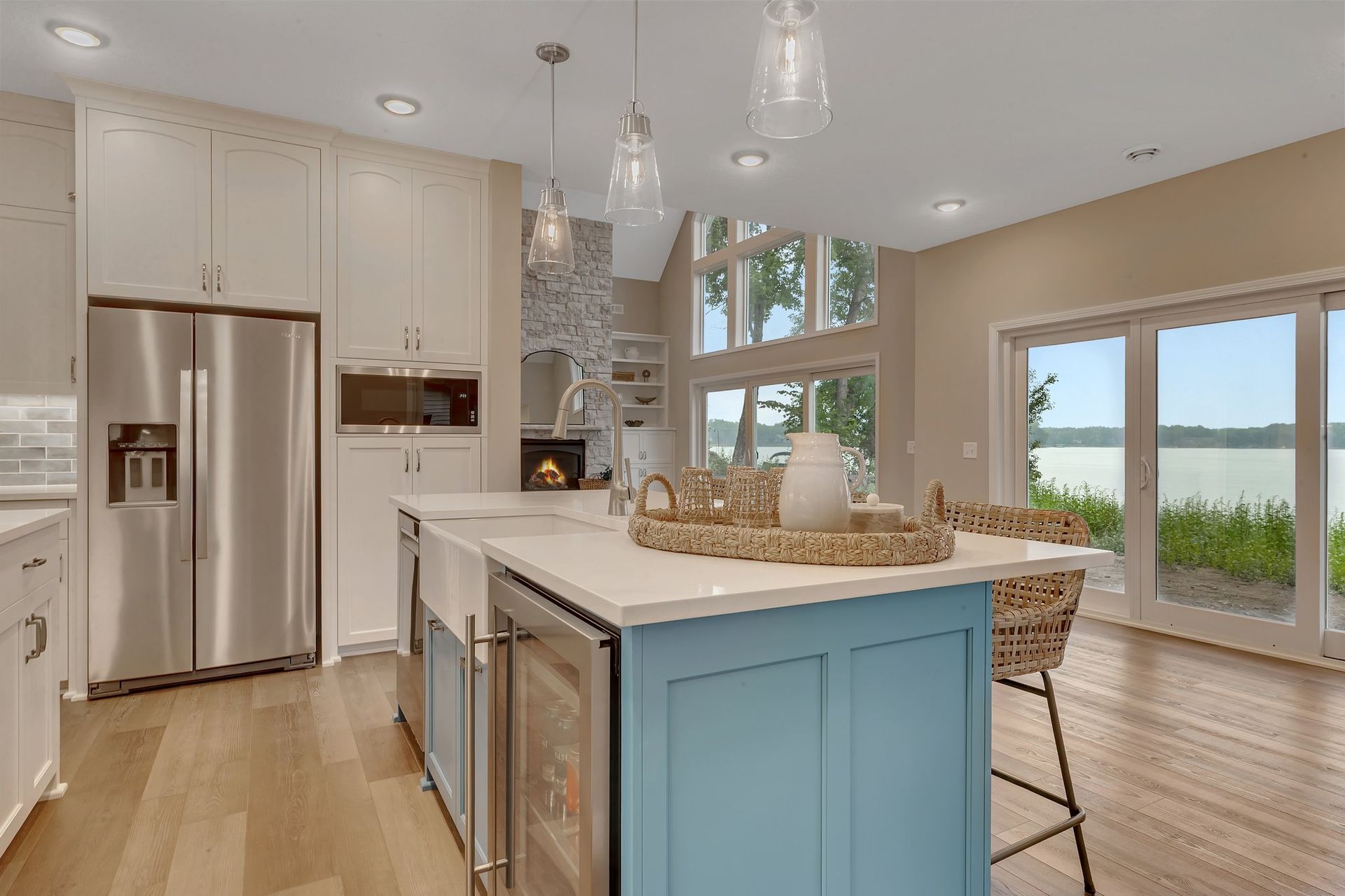 A kitchen with white cabinets , stainless steel appliances , a blue island and a view of the water.