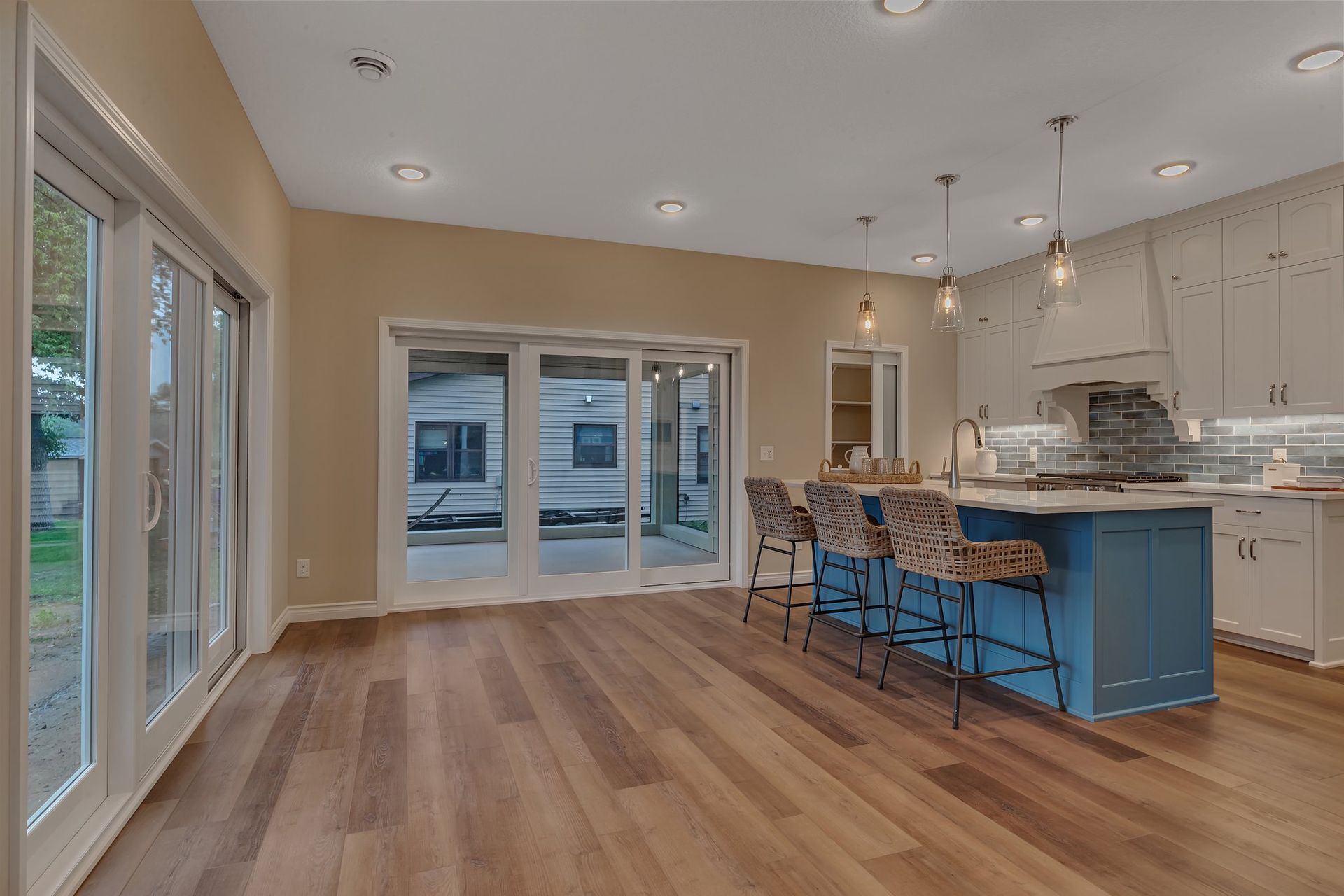 A kitchen with hardwood floors , white cabinets , a blue island and sliding glass doors.