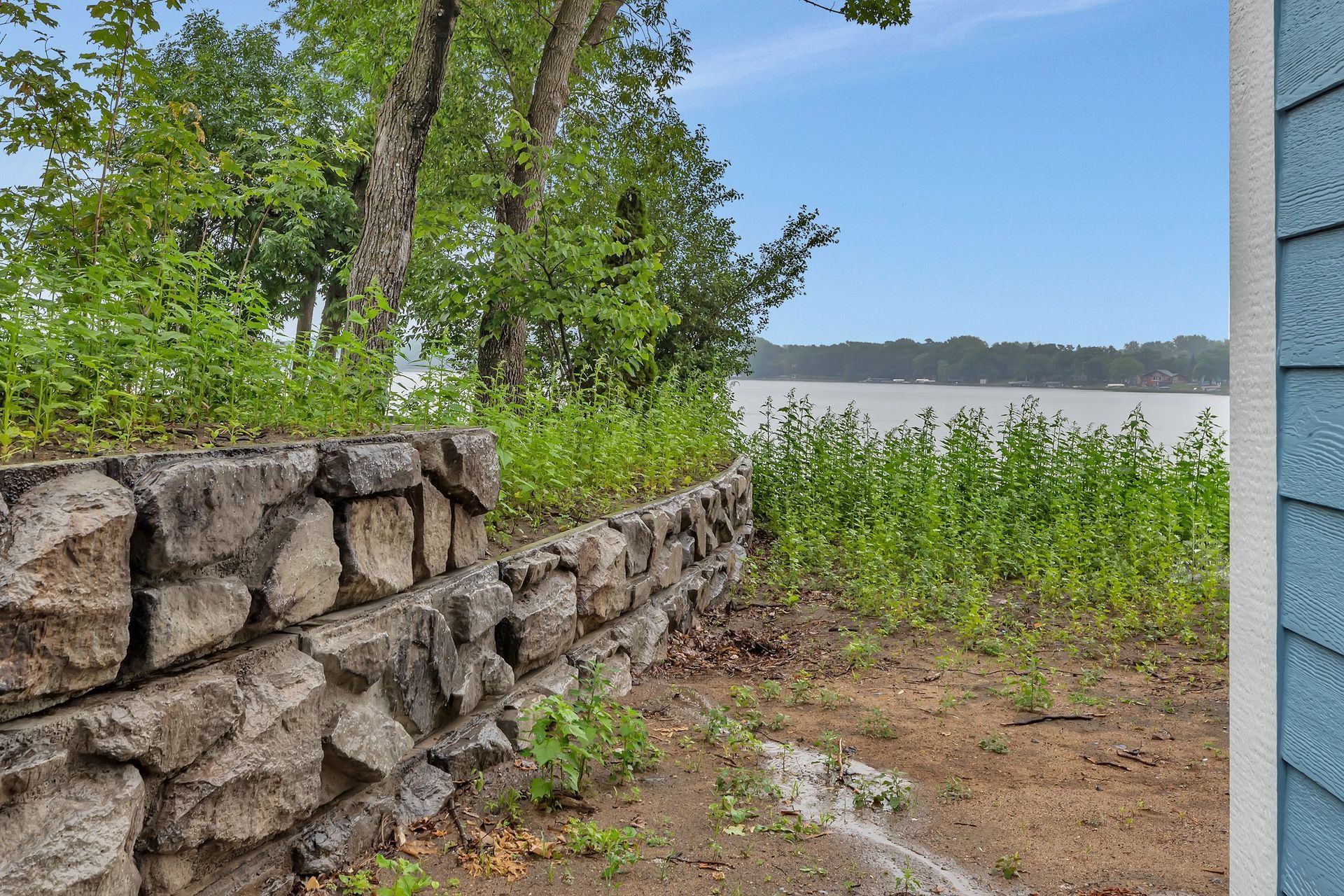 A stone wall next to a house with a view of a lake.