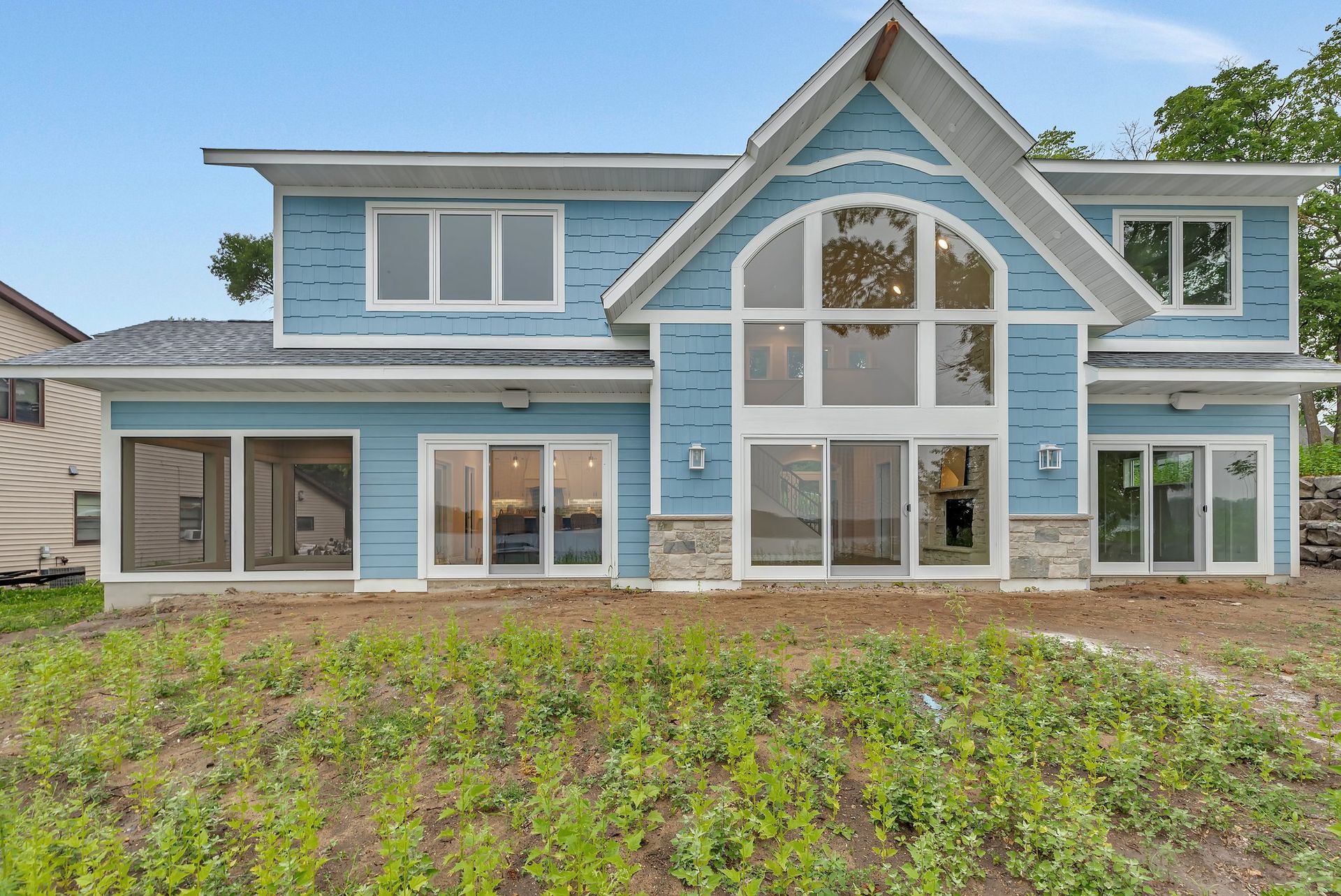 A large blue house with a lot of windows is sitting on top of a lush green field.