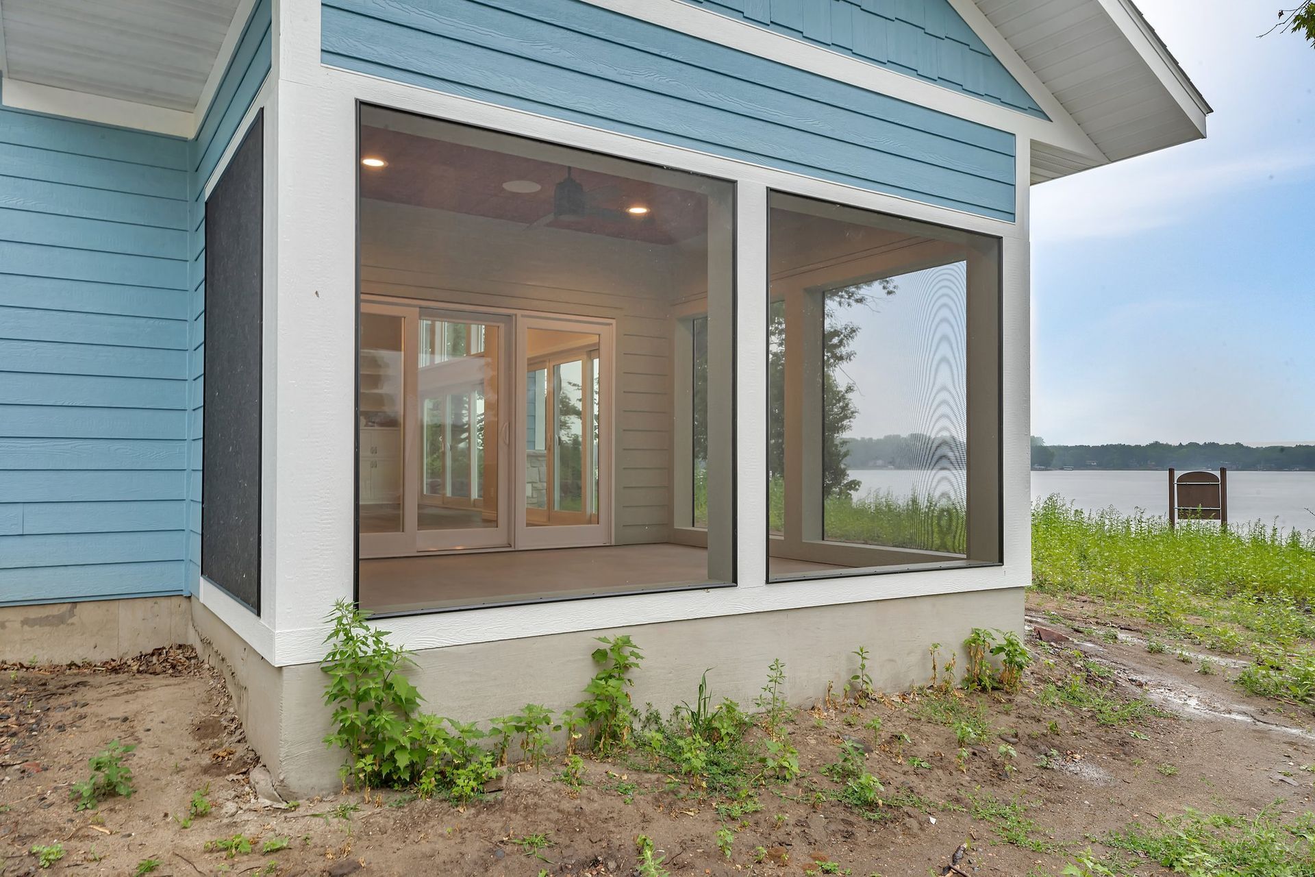 A blue house with a screened in porch overlooking a lake.