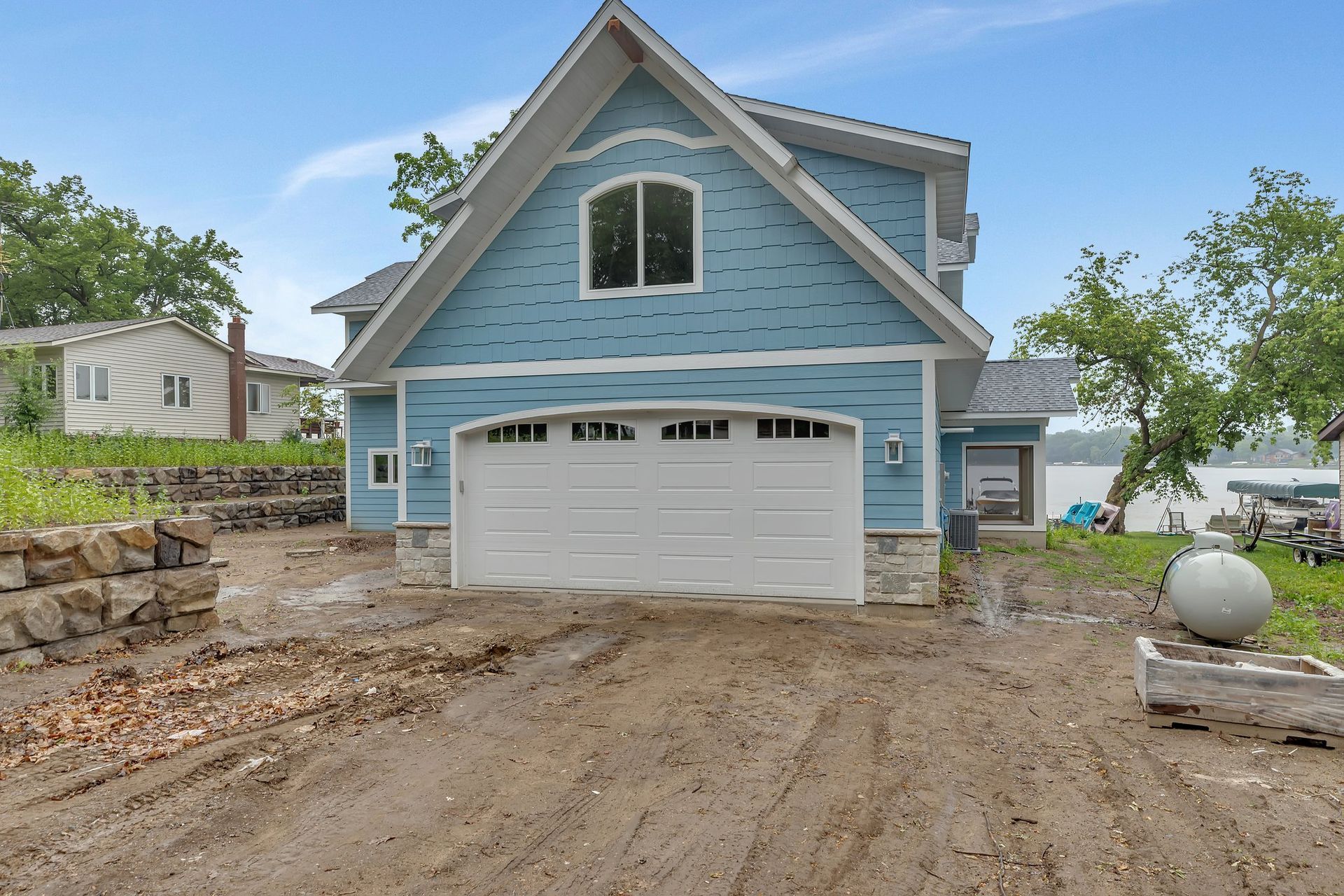 A blue house with a white garage door is sitting on top of a dirt field.
