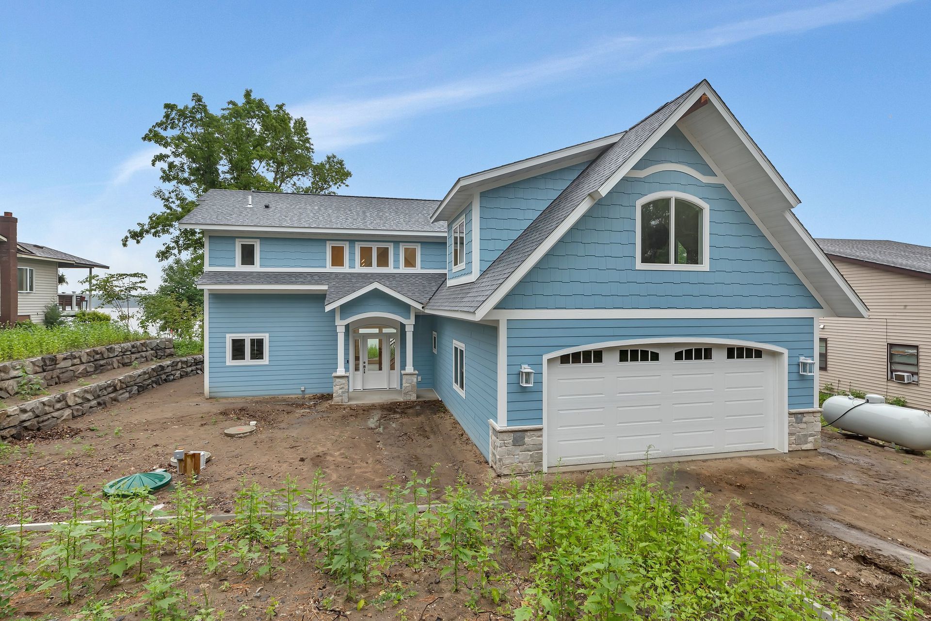 A large blue house with a white garage door is sitting on top of a dirt hill.
