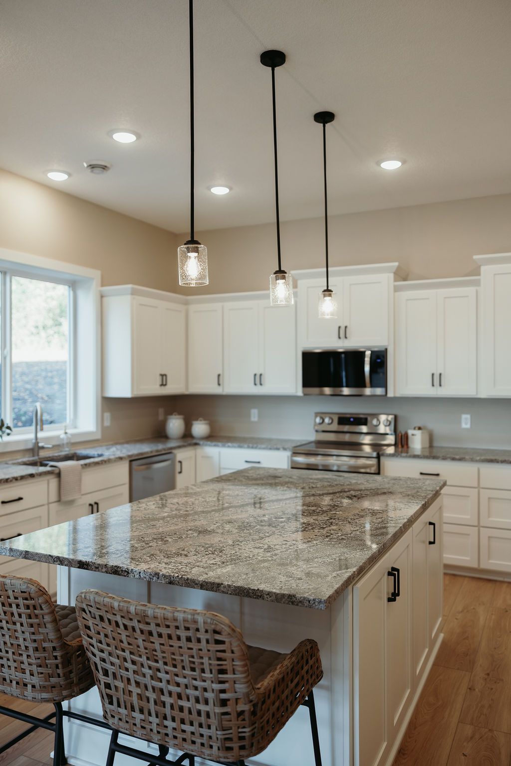 Modern kitchen with white cabinets, granite island, and pendant lights.