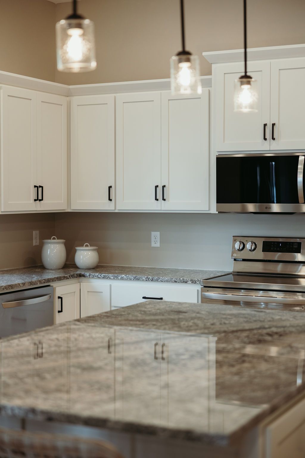 White kitchen with granite countertops, white cabinets, and pendant lights.