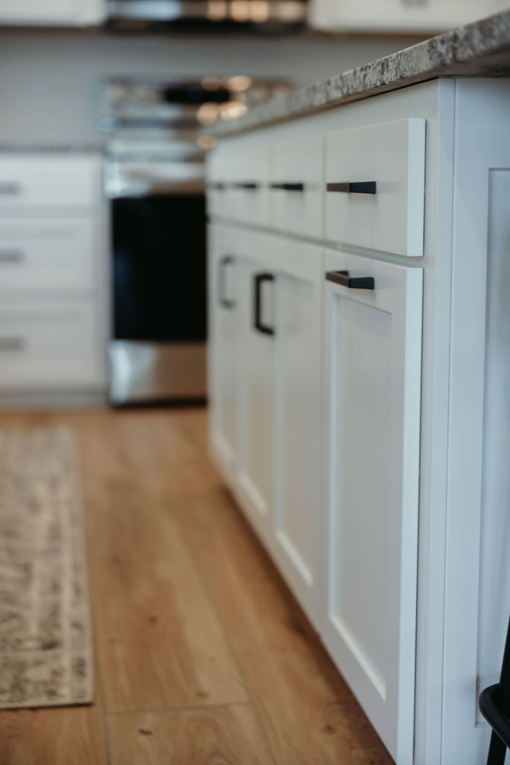 White kitchen cabinets with black handles, a stainless steel oven, and wooden floor.