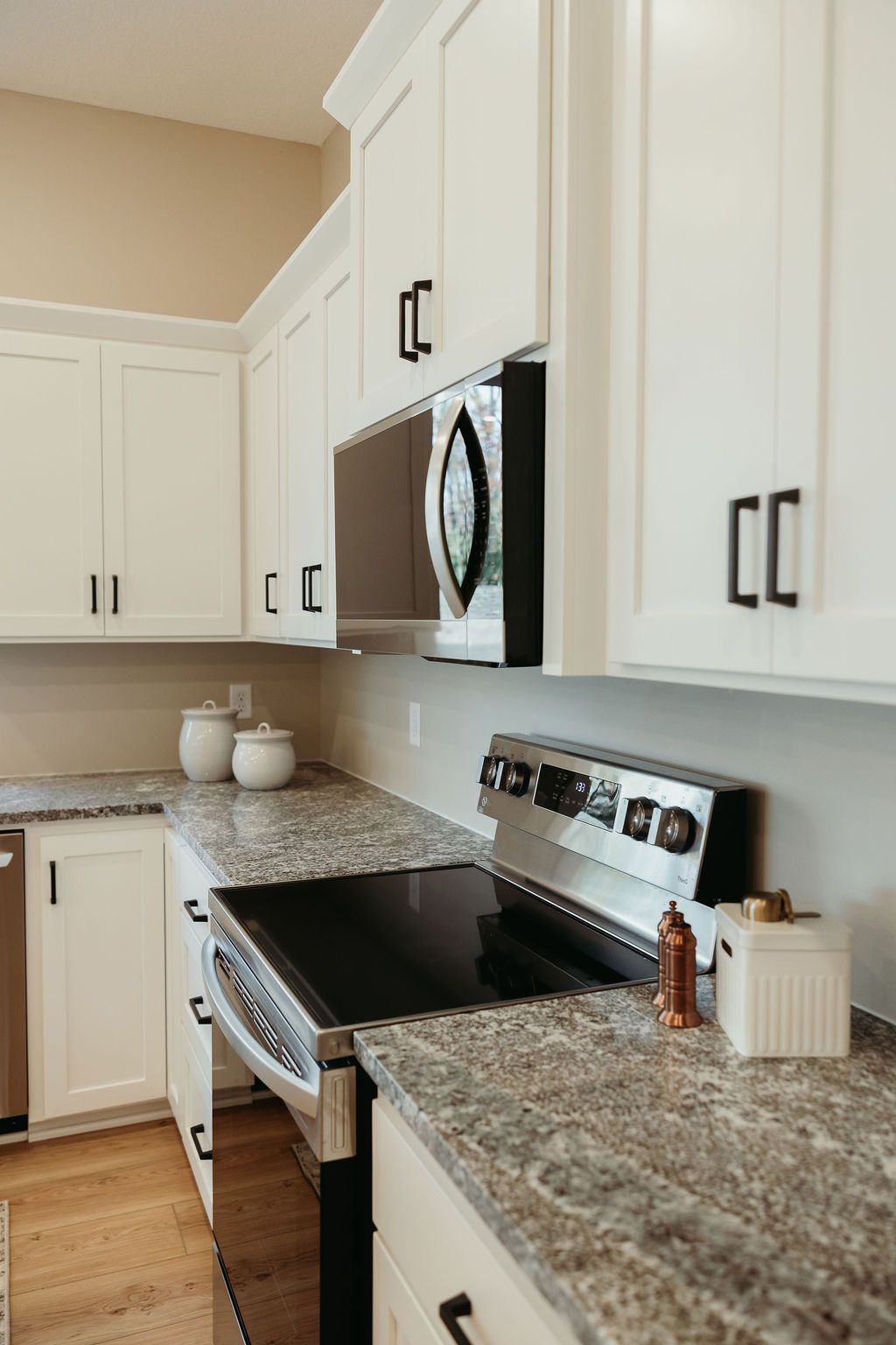 White kitchen cabinets with black hardware above a stovetop and granite countertop.