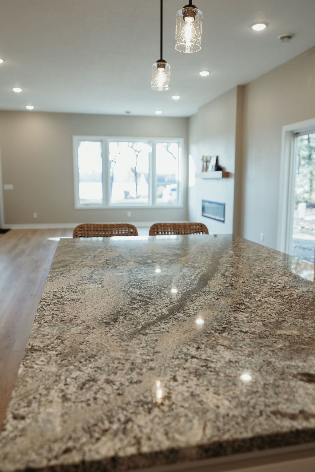 Kitchen island with granite countertop, pendant lights, and view of living area with fireplace and windows.