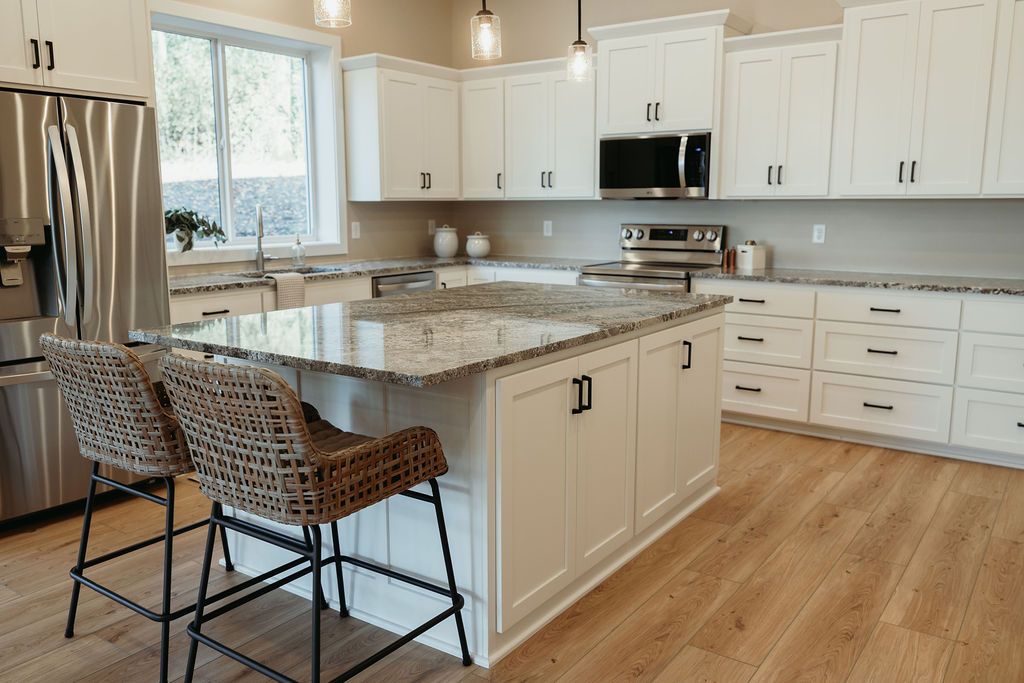 Modern white kitchen with island, stainless steel appliances, and wood flooring. Two bar stools.