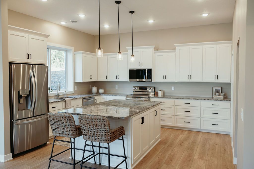 Modern kitchen with white cabinets, granite island, stainless steel appliances, and wood flooring.