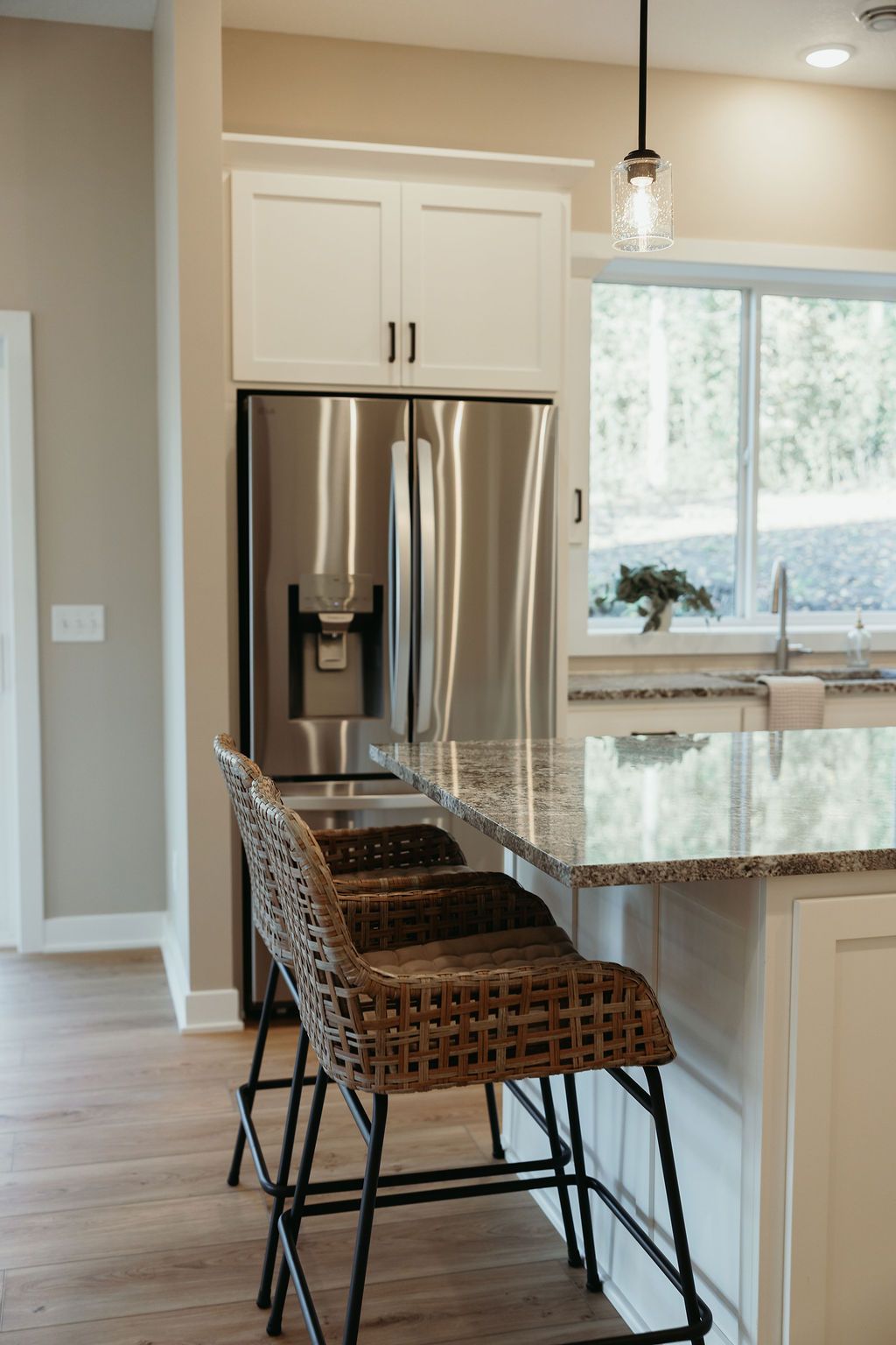 Kitchen with stainless steel refrigerator, granite countertop, and woven bar stools.