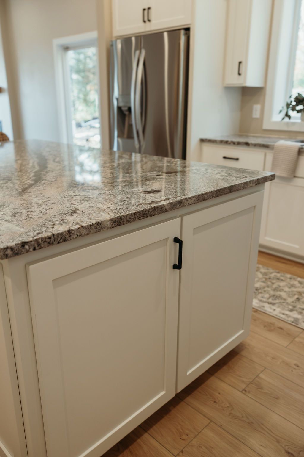 Kitchen island with granite countertop, white cabinets, and stainless steel refrigerator in the background.