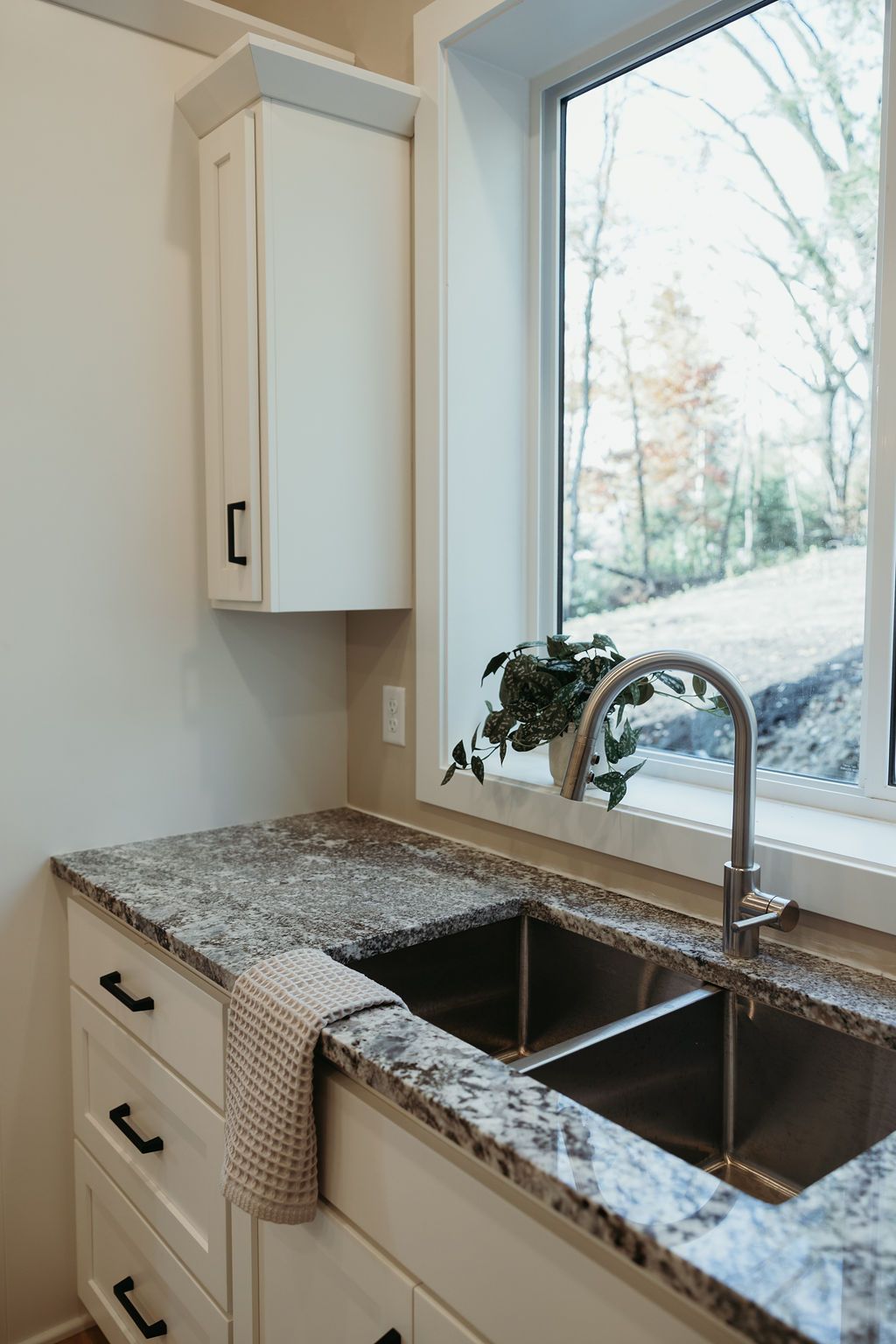 Kitchen sink with granite countertop, white cabinets, and a window overlooking greenery.