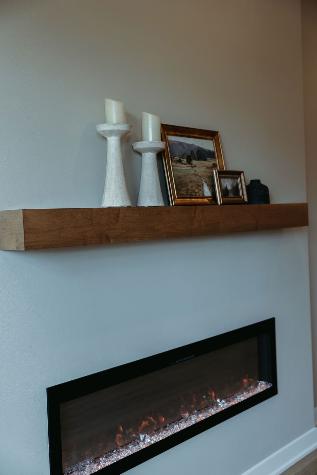 Floating wooden shelf with candles and framed photos above a slanted fireplace.