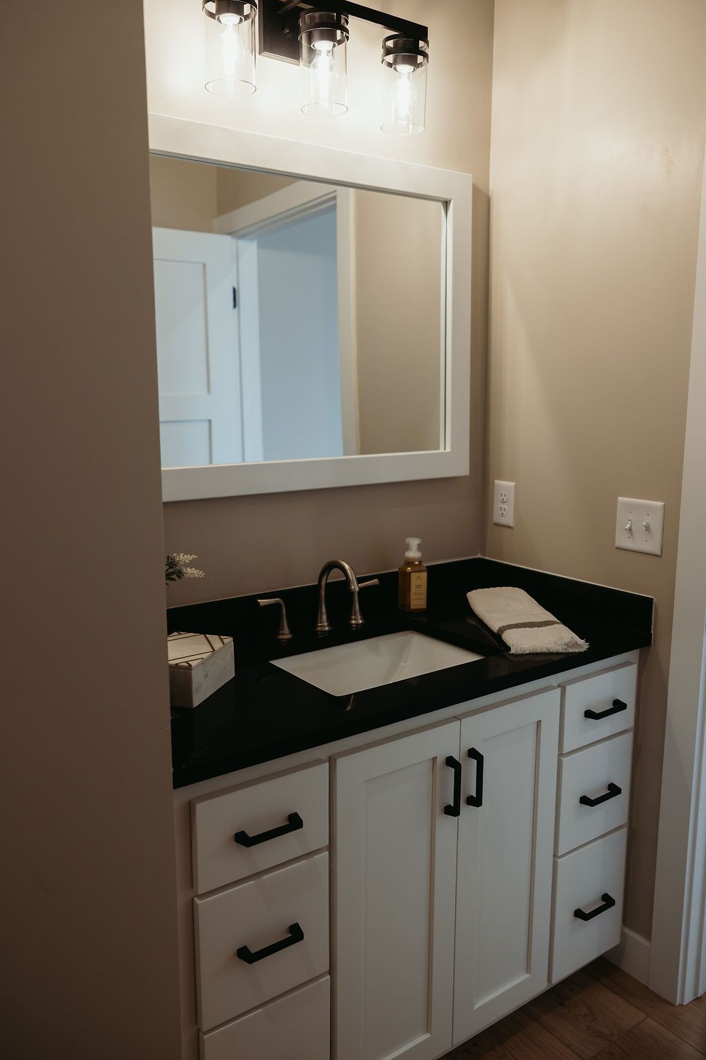 Bathroom with white vanity, black countertop, rectangular mirror, and light fixture.