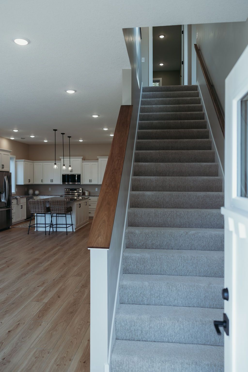 Interior view of a modern home with a staircase, kitchen, and light-colored wood floors.