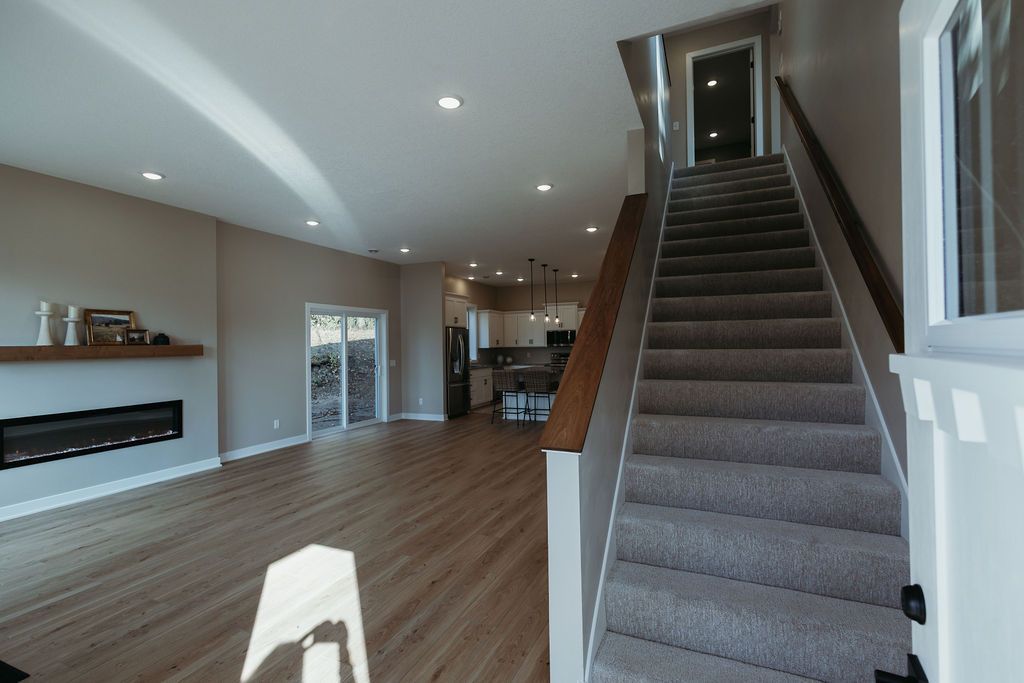 Spacious, modern home interior with staircase and living area. Light wood floors, fireplace, and sliding doors.