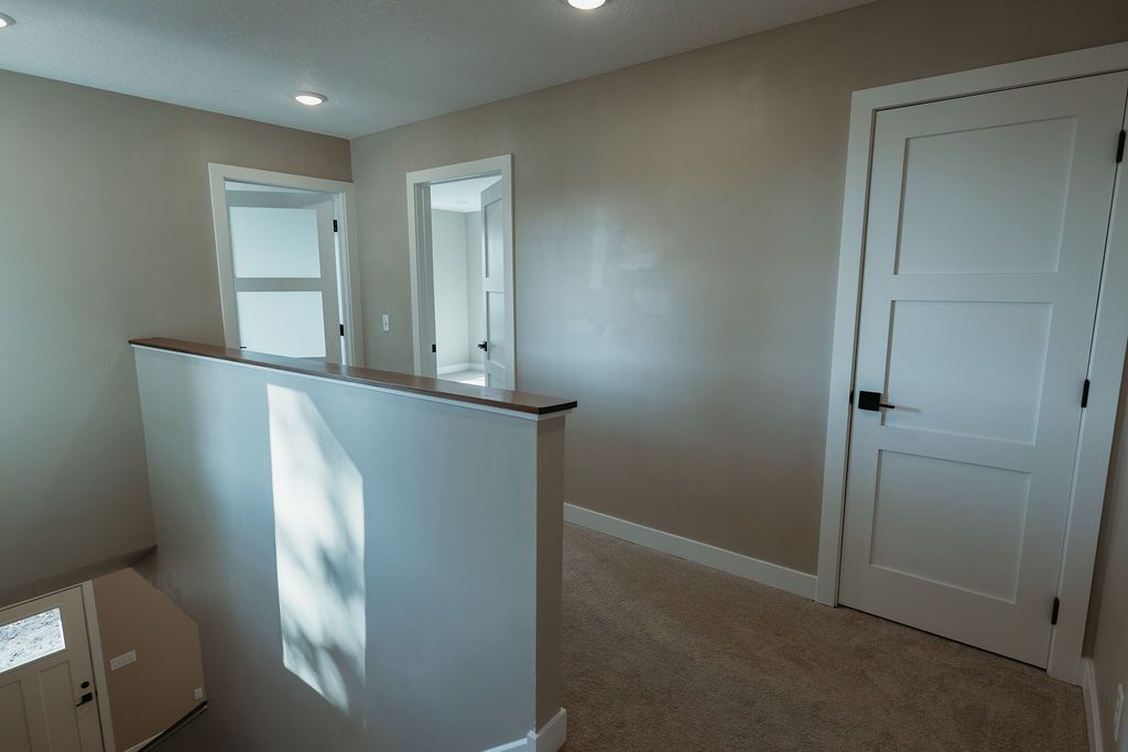 Hallway with doors, carpeted floor, and a railing with natural light from a window.
