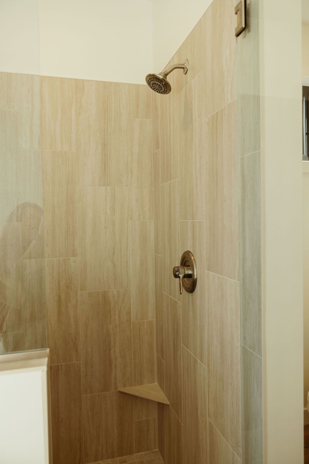 Shower stall with tan vertical tile, bronze showerhead and faucet, and a small built-in bench.