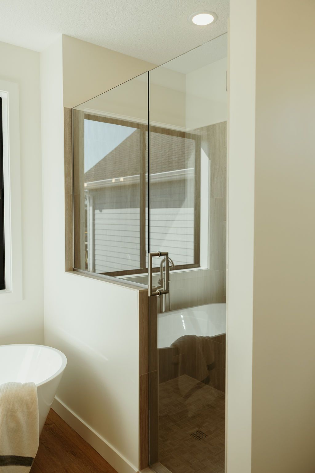 A bathroom with a glass shower enclosure and a bathtub; a window is behind the bathtub.